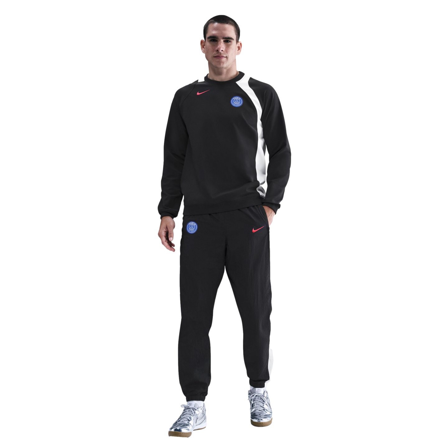 Man wearing a black Nike Paris Saint-Germain tracksuit and silver sneakers against a black background.