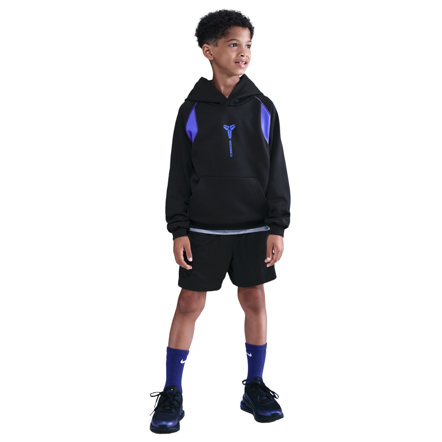A young boy wearing a black and purple hoodie, black shorts, and purple socks stands against a solid black background.