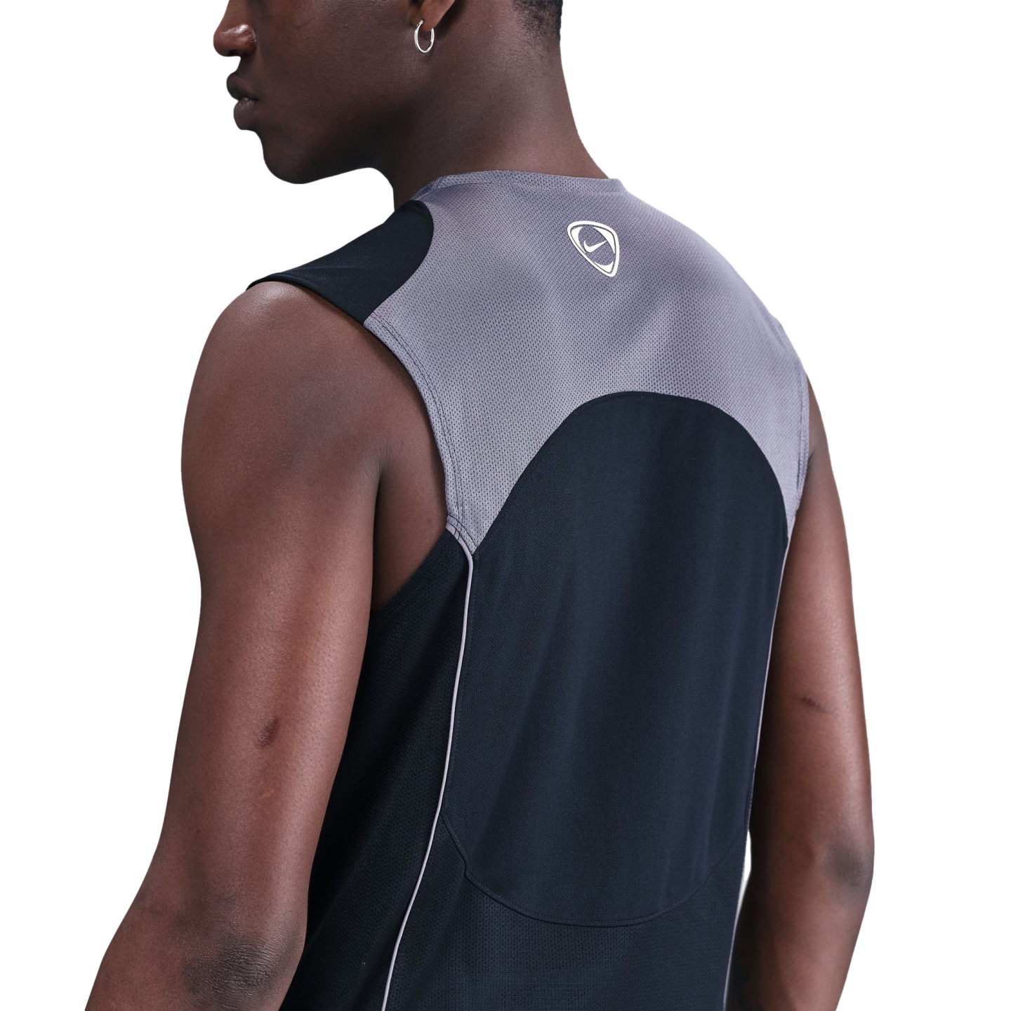 Back-angle view of a person wearing a grey and black Nike sleeveless mesh athletic top, set against a solid black background.