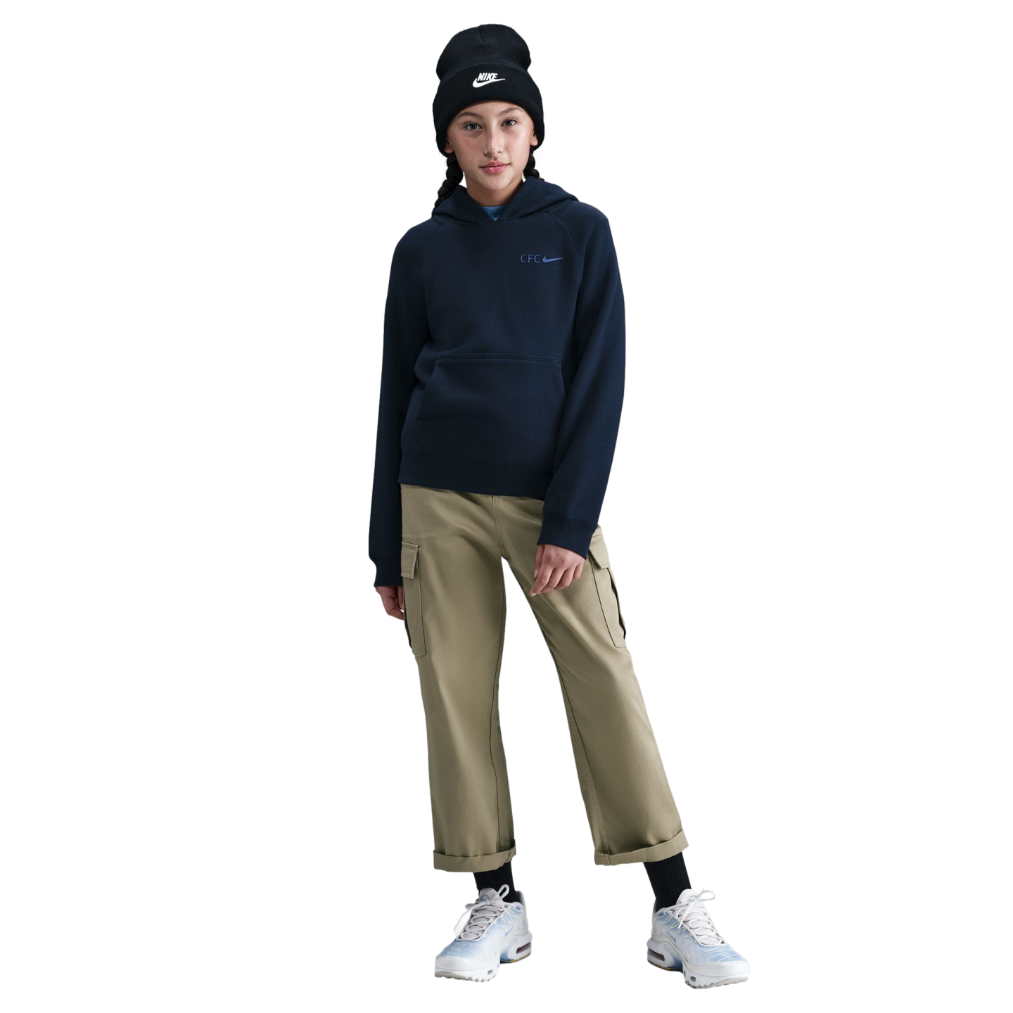 A person wearing a black Nike beanie, navy Nike "CFC" hoodie, tan cargo pants, and light blue sneakers, standing against a black background.