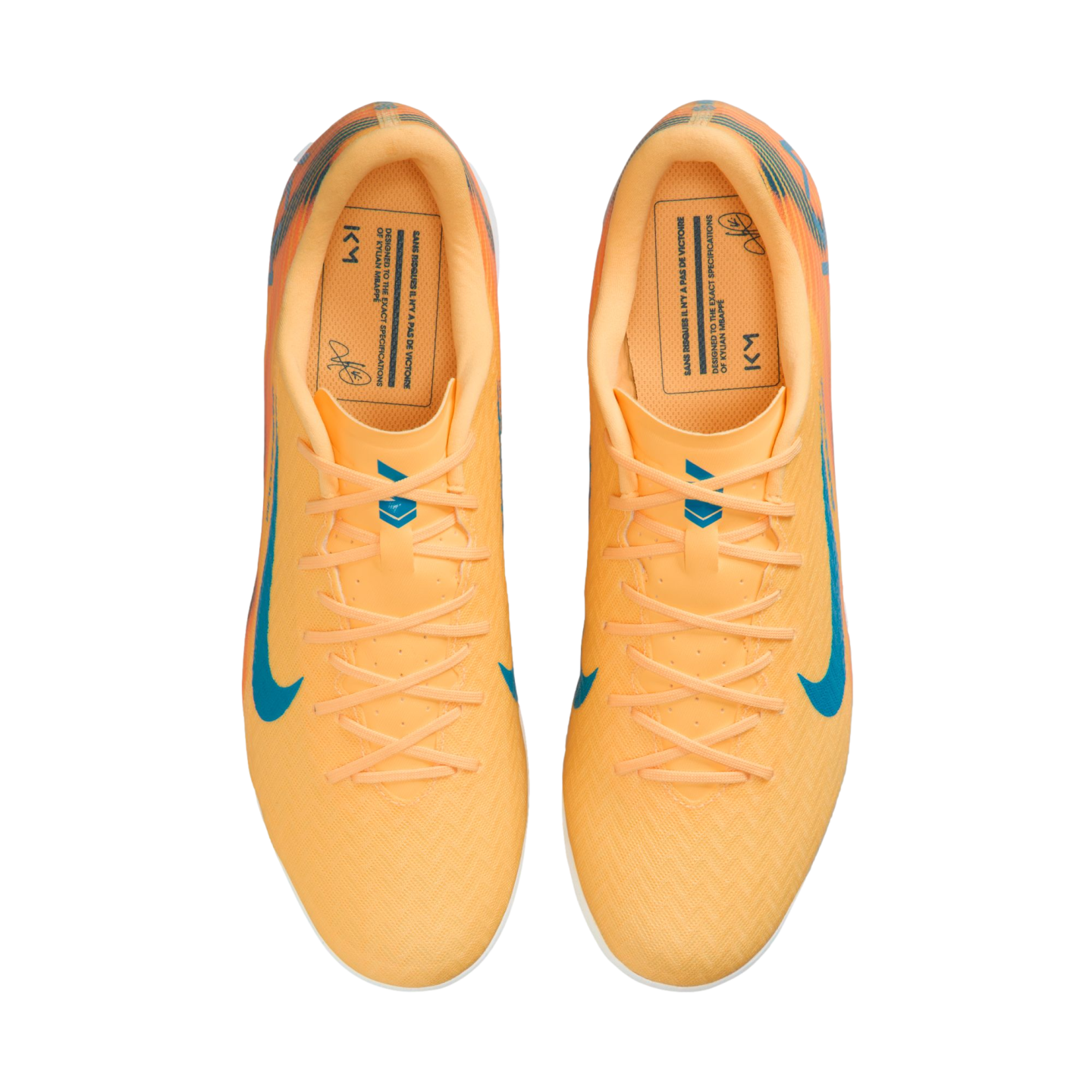 Top-down view of bright orange Nike soccer shoes with blue swooshes and Kylian Mbappé "KM" branding on the insoles.