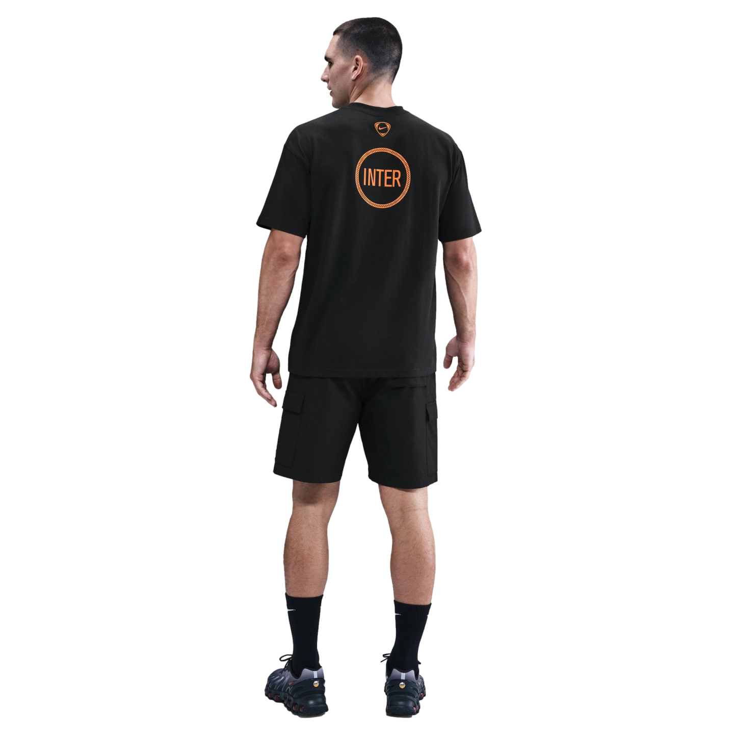 Rear view of a man wearing a black Nike Inter Milan T-shirt with orange graphics, black cargo shorts, and black sneakers on a plain black background.