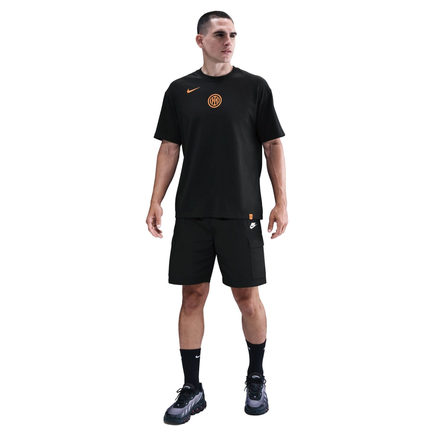 Man standing in a black Nike Inter Milan t-shirt with orange logos, black cargo shorts, and black sneakers against a solid black background.