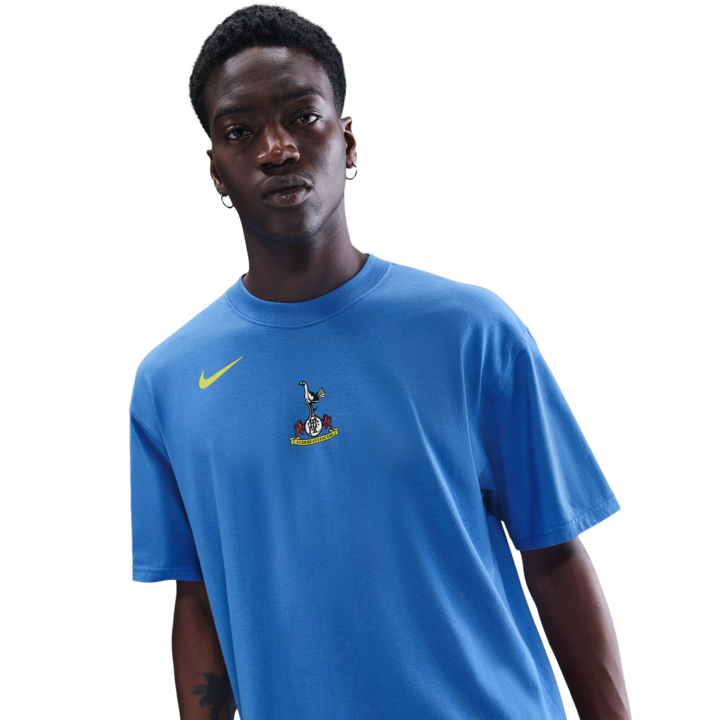 A man wearing a blue Nike t-shirt with a Tottenham Hotspur crest, against a black background.