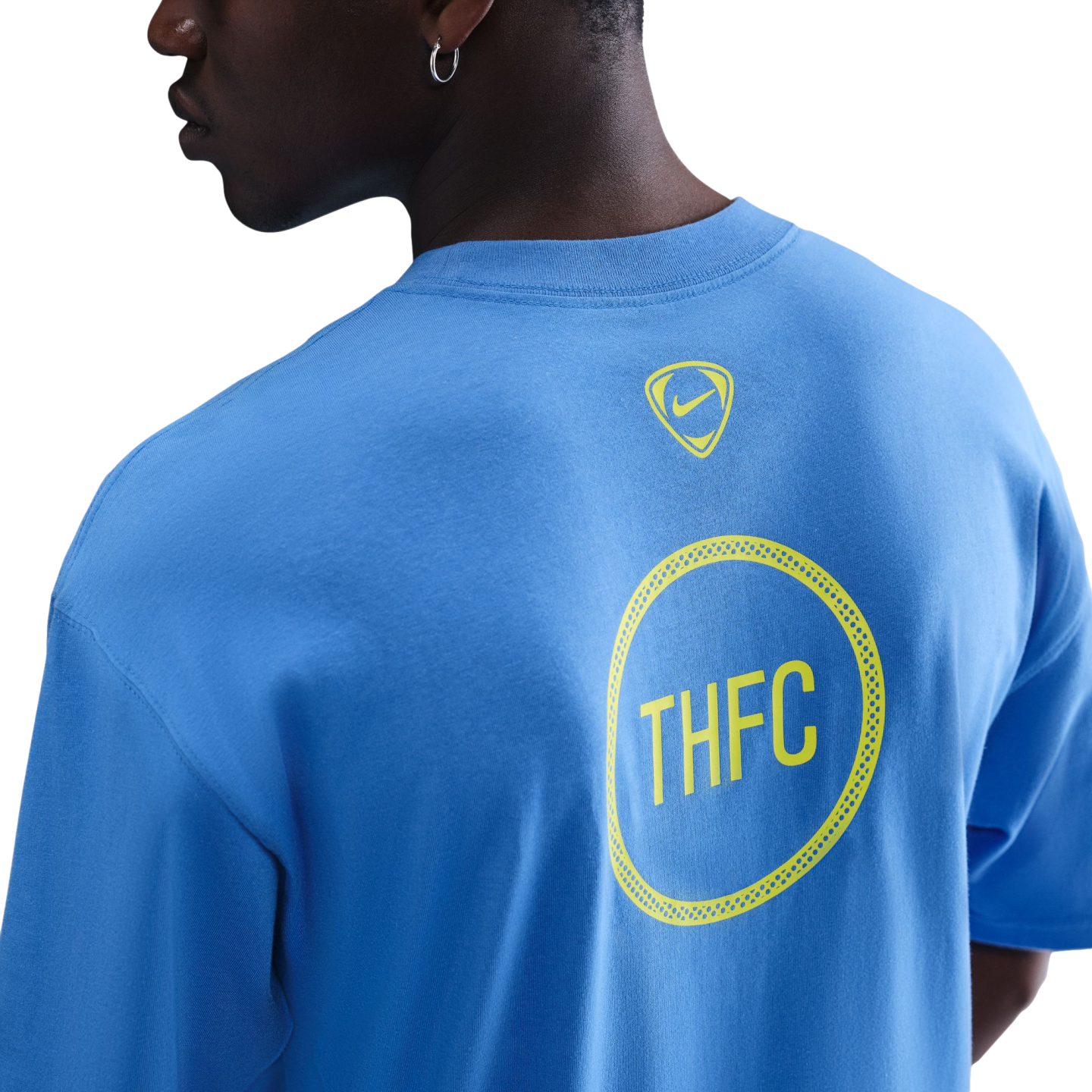 Back view of a person in a light blue t-shirt featuring a small yellow Nike logo and a larger yellow circular "THFC" graphic.
