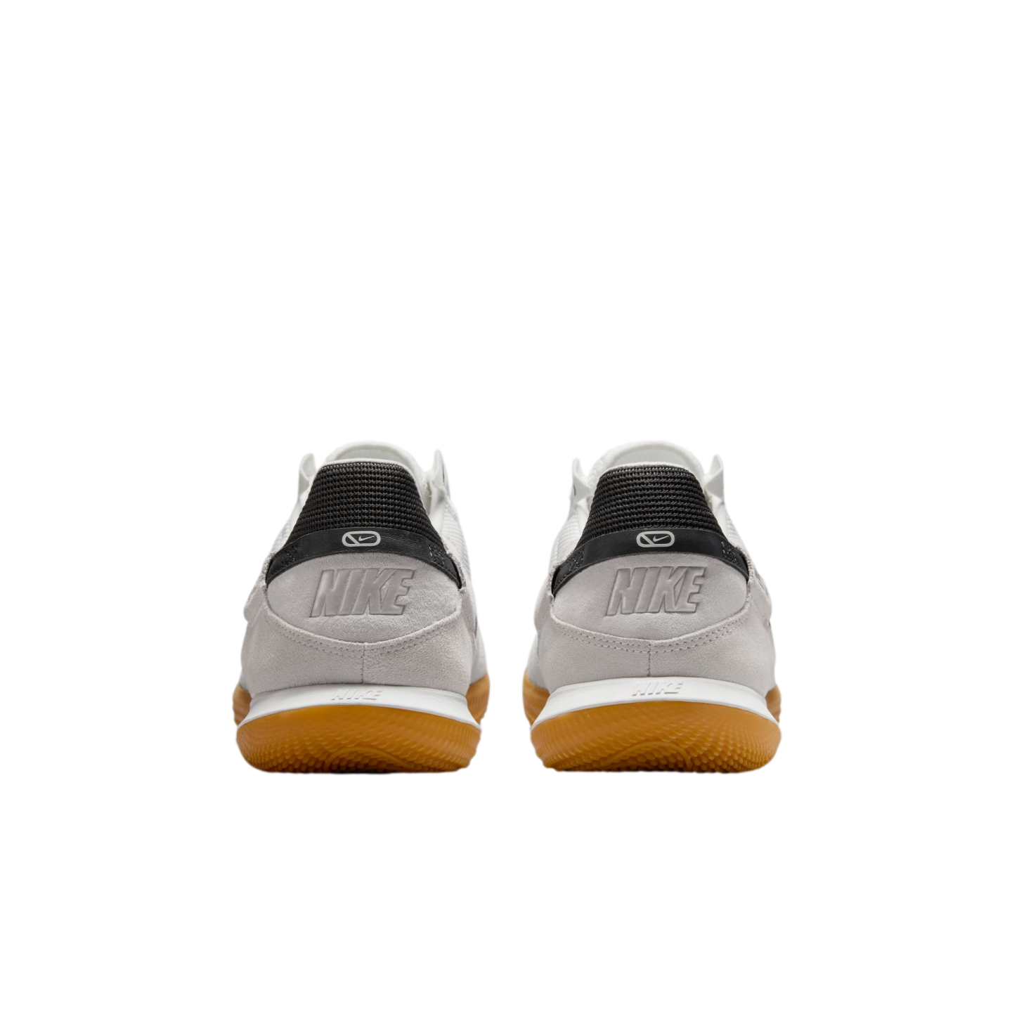 A rear view of light grey Nike sneakers featuring white midsoles, brown gum outsoles, and "NIKE" embossed on the suede heel panels below black textured tabs.