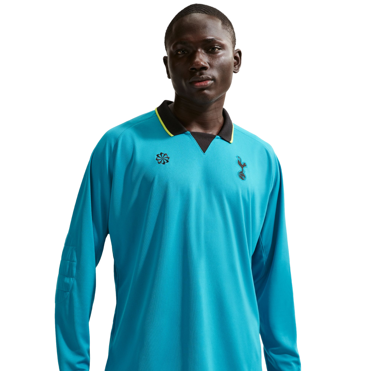 A man wearing a long-sleeved, bright blue Tottenham Hotspur soccer jersey with a black and yellow collar, set against a black background.