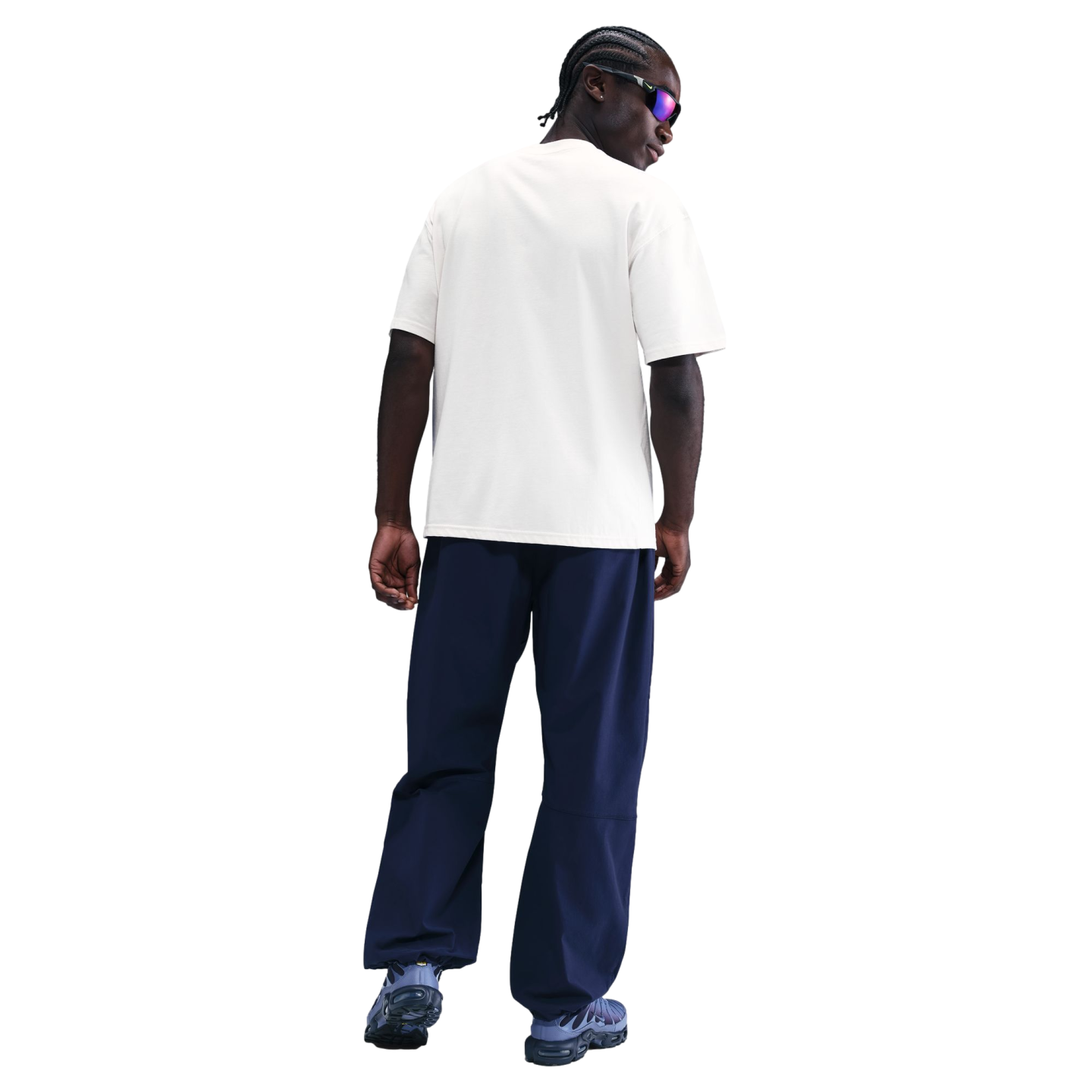 Rear view of a person with braids wearing a white T-shirt, navy baggy pants, and blue sneakers against a solid black background.