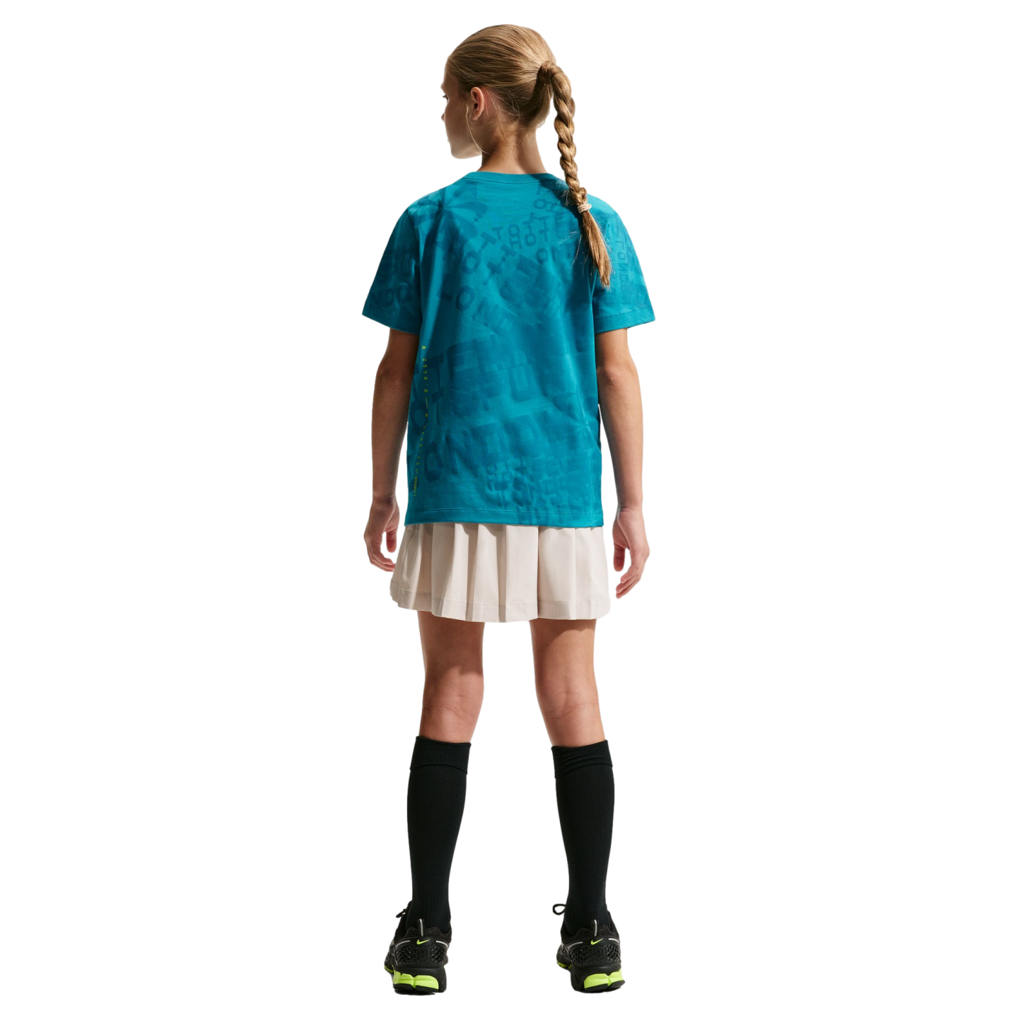 Back view of a girl with a blonde braid wearing a teal patterned t-shirt, beige pleated skirt, black knee-high socks, and black sneakers against a black background.