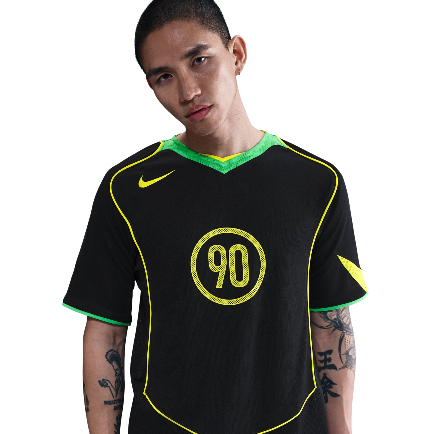 A man with arm tattoos wears a black Nike Total 90 jersey with neon green and yellow accents, set against a plain white background.