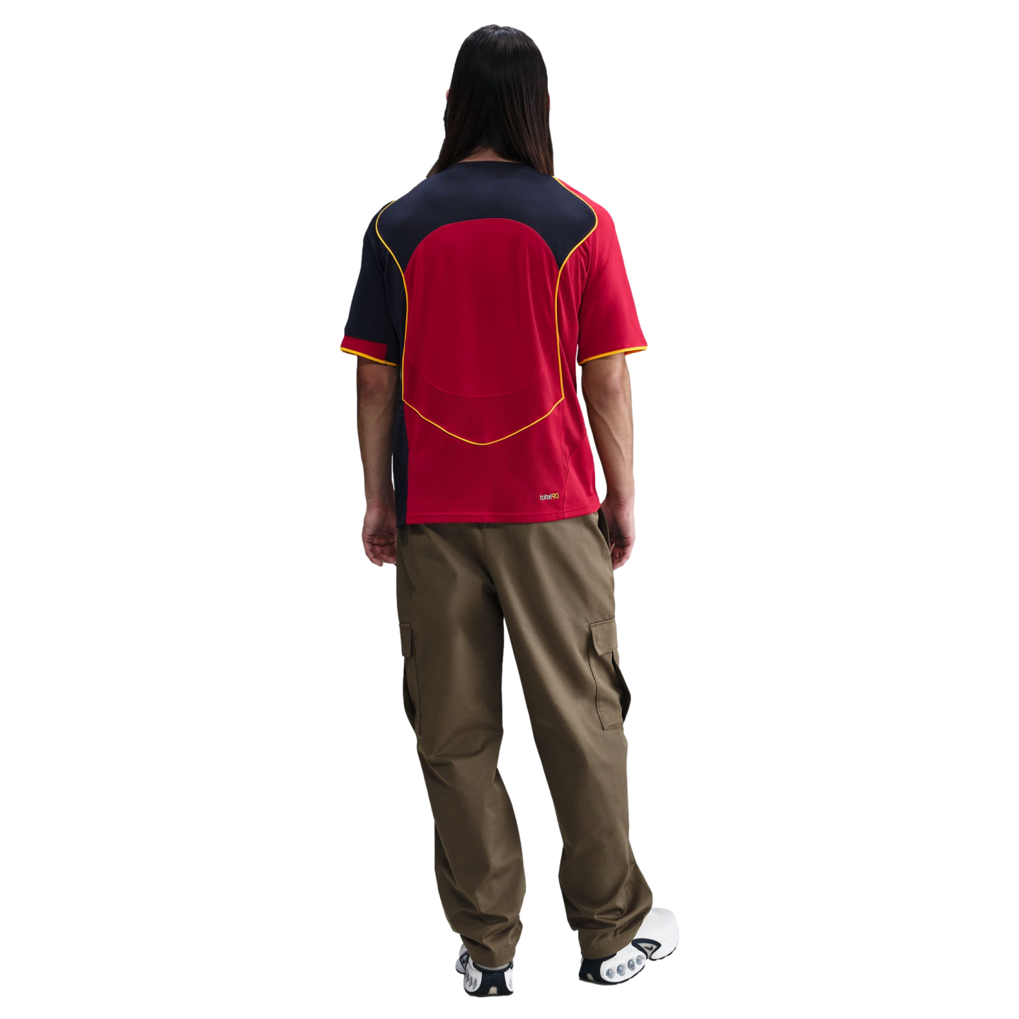 Back view of a person with long dark hair wearing a red, black, and yellow jersey, olive green cargo pants, and white and black sneakers on a white background.