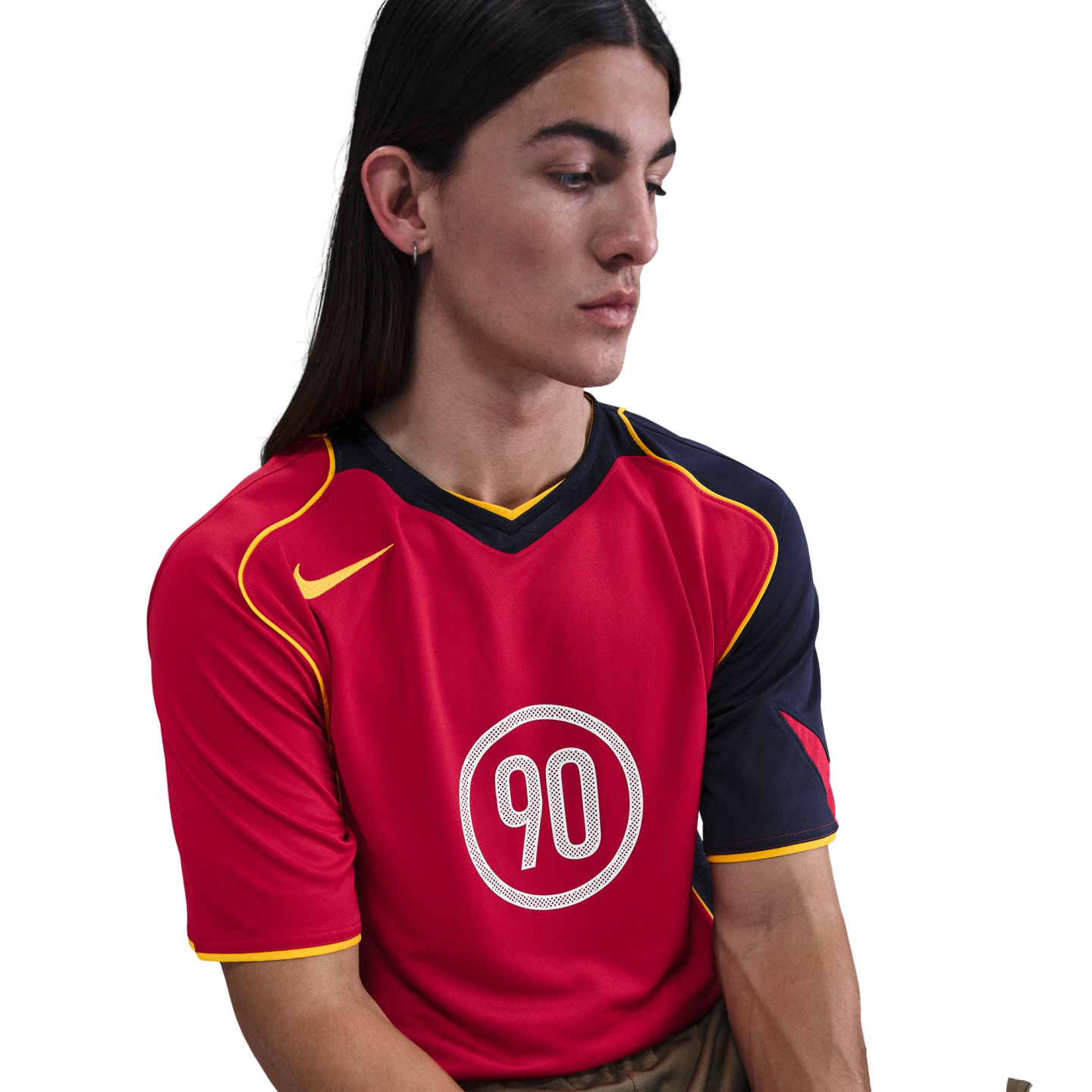 A person with long dark hair wearing a red and navy Nike Total 90 sports jersey with yellow trim, looking down against a white background.