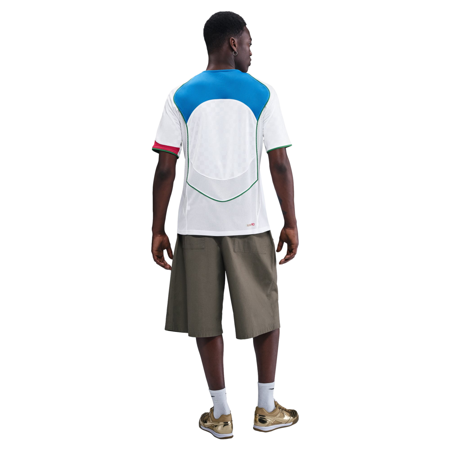 Rear view of a man wearing a white and blue soccer jersey, olive green shorts, white socks, and metallic gold sneakers against a plain white background.