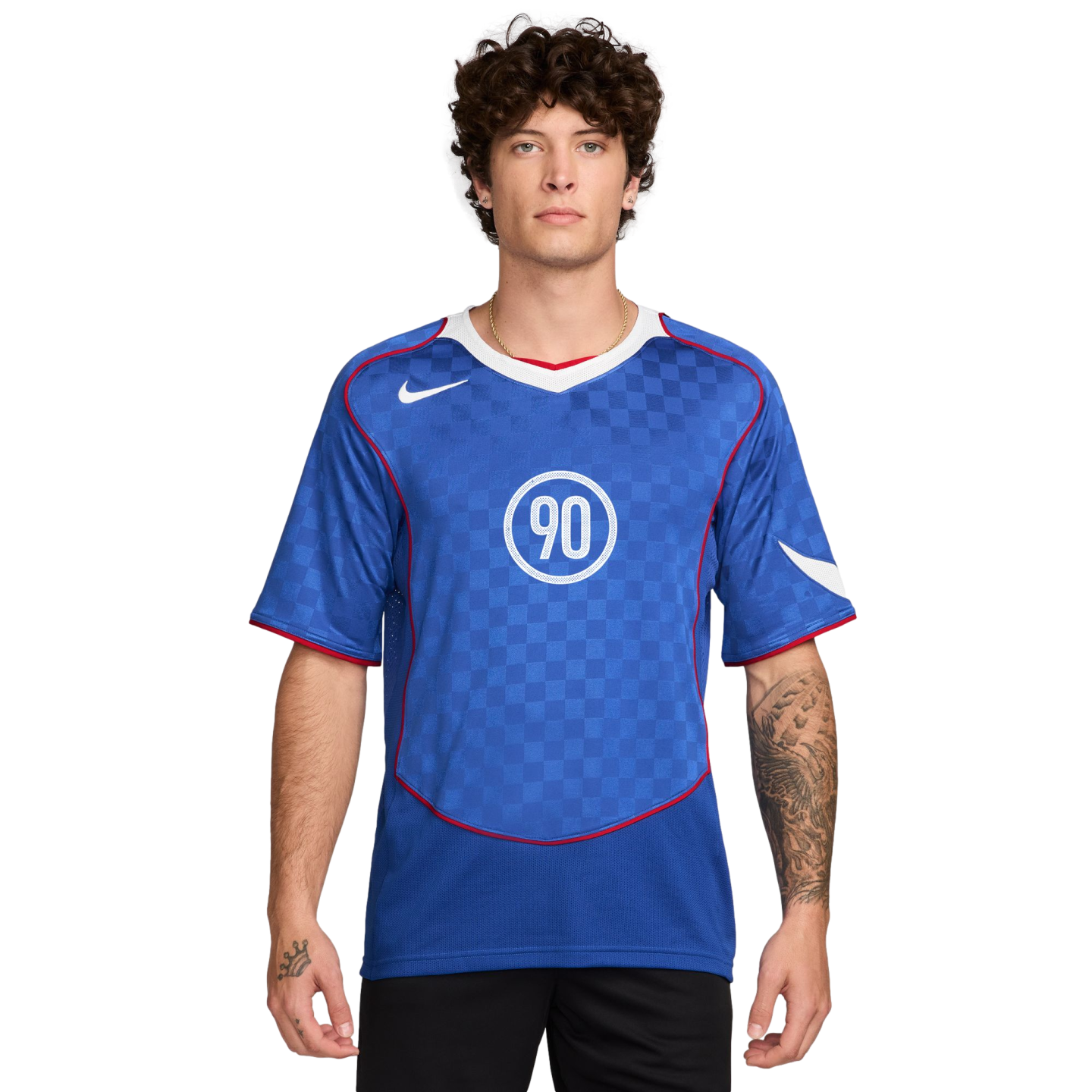 A man with curly hair wearing a blue Nike Total 90 soccer jersey with a white "90" logo and checkered pattern.