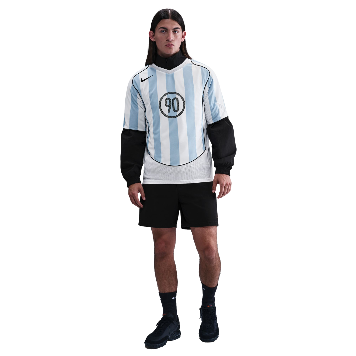 A male model wears a light blue and white striped Nike jersey over a black top, with black shorts and sneakers, posed against a plain white background.