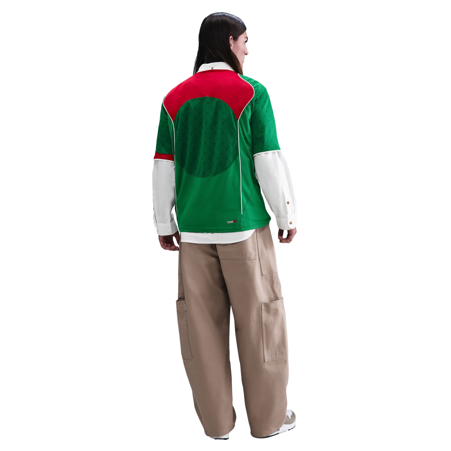 Back view of a person wearing a green and red mesh jersey over a white button-down shirt, baggy tan cargo pants, and white sneakers against a white background.