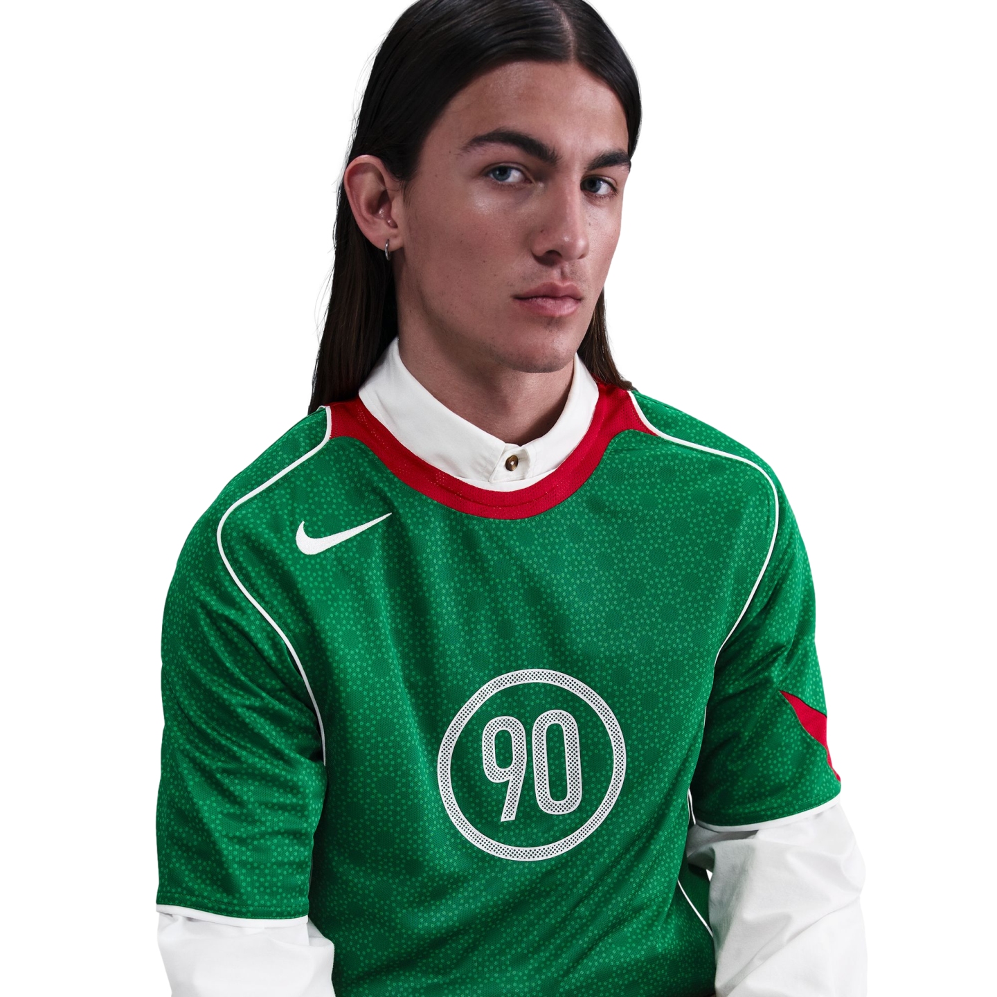 A person with long dark hair wearing a green Nike Total 90 jersey layered over a white collared shirt.