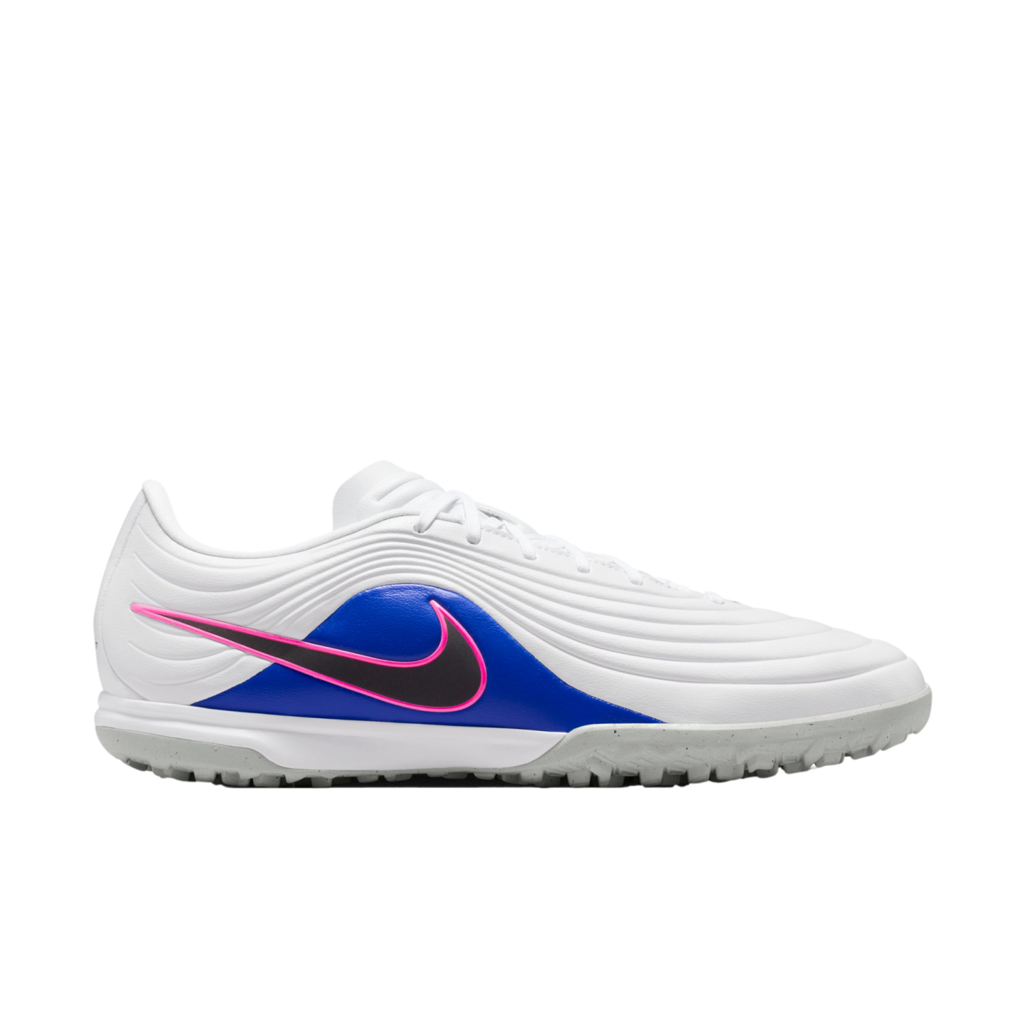 Profile view of a white Nike turf soccer shoe with a wavy textured upper, blue side panel, and black Swoosh outlined in pink. Set against a black background.