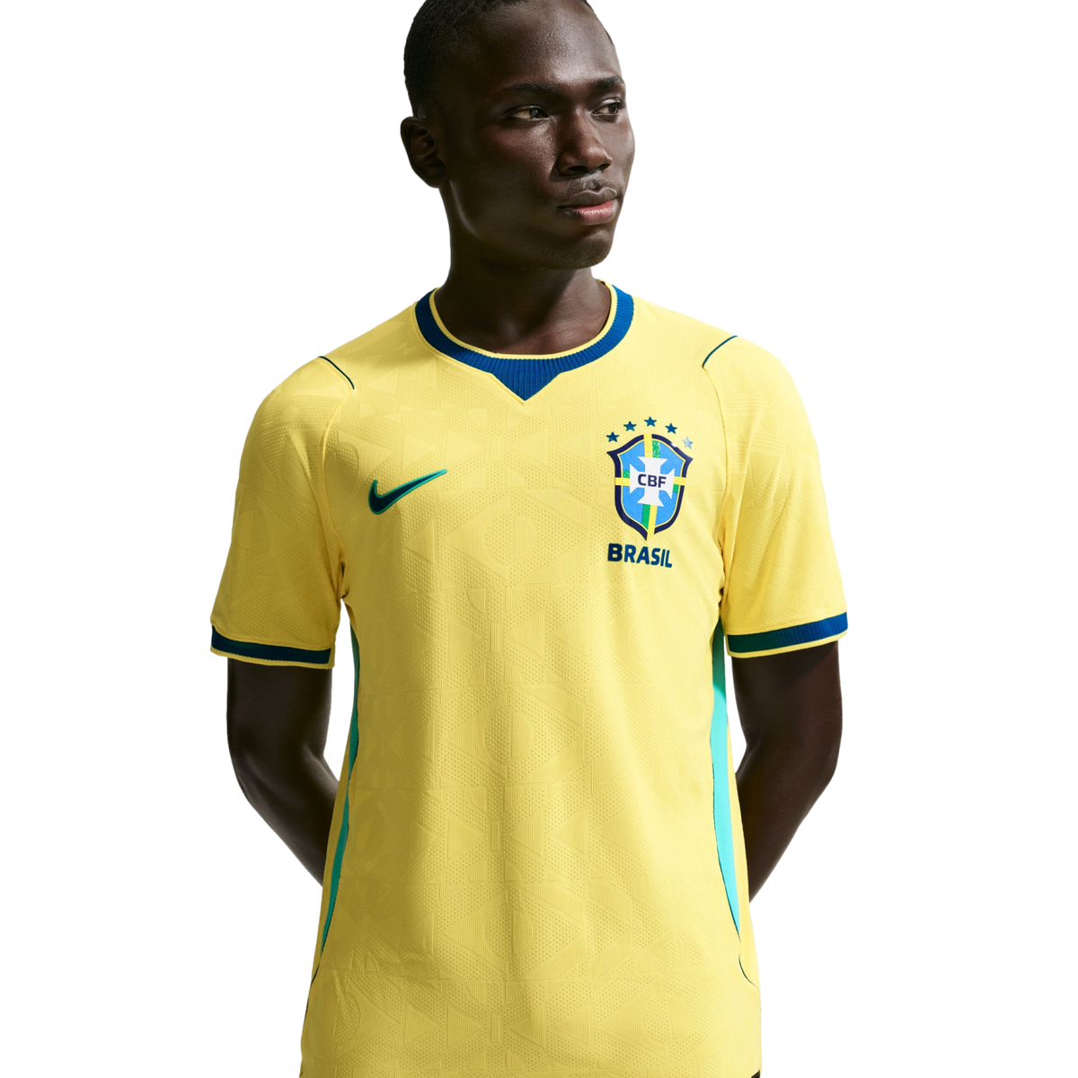 A young Black man wearing a yellow Nike Brazil national football team home jersey with blue trim, standing against a solid black background.