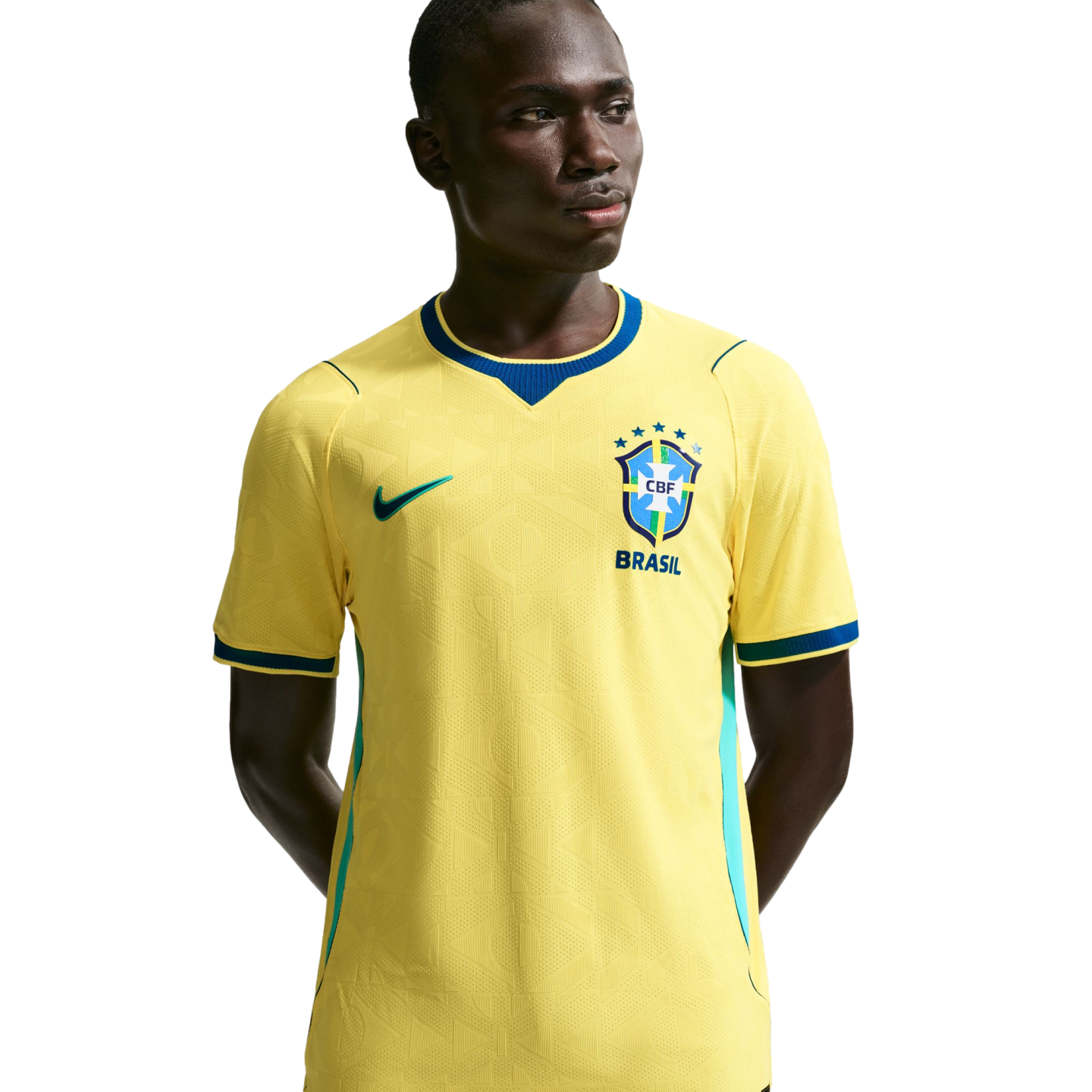 A young Black man wearing a yellow Nike Brazil national football team home jersey with blue trim, standing against a solid black background.