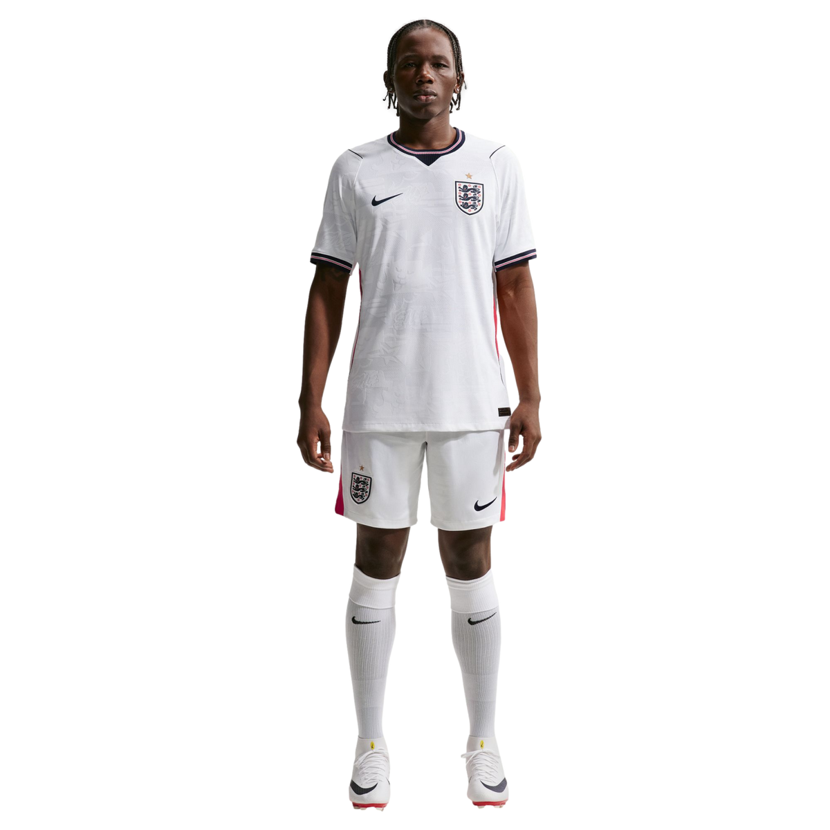 A full-body photograph of a male athlete standing against a solid black background, wearing the white Nike England national team home soccer kit. The kit includes a white jersey and shorts featuring the team's Three Lions crest and Nike logo, paired with