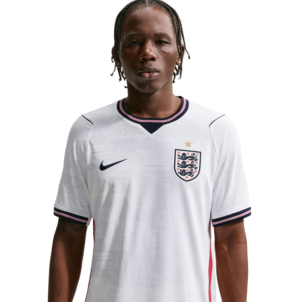 A waist-up portrait of a young man with braided hair wearing a white Nike England national football team home jersey against a solid black background.