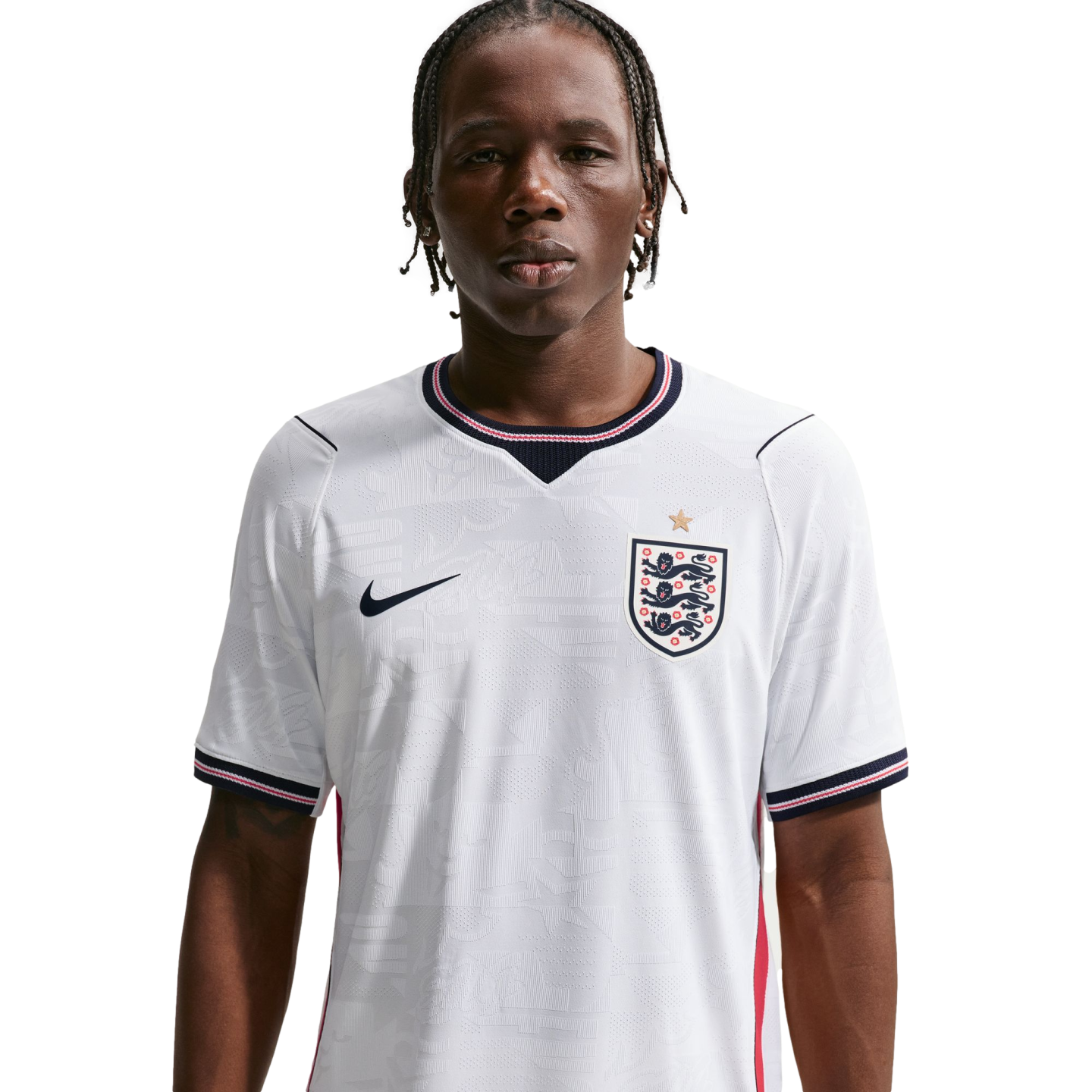 A waist-up portrait of a young man with braided hair wearing a white Nike England national football team home jersey against a solid black background.