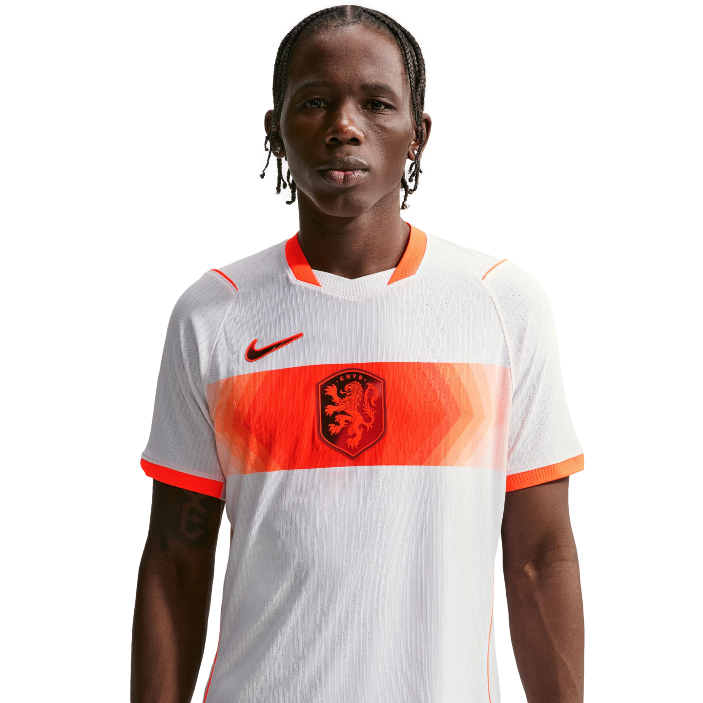 A young man with braided hair wears a white Netherlands national football team away jersey with a horizontal orange patterned band, the KNVB lion crest, and a black Nike swoosh, set against a solid black background.