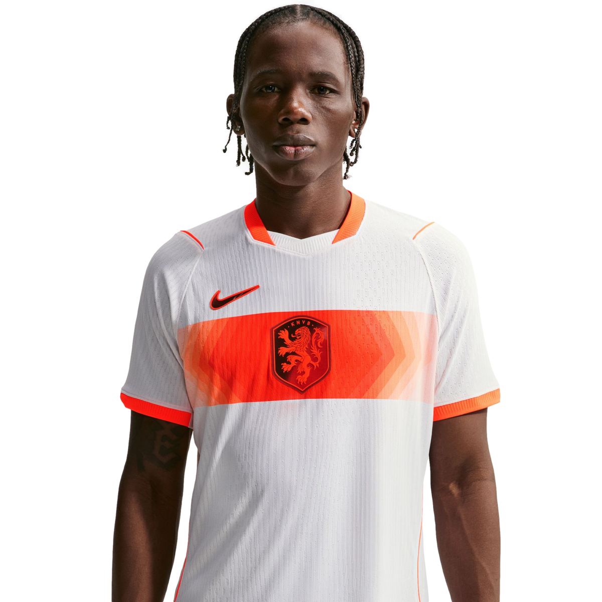 A young man with braided hair wears a white Netherlands national football team away jersey with a horizontal orange patterned band, the KNVB lion crest, and a black Nike swoosh, set against a solid black background.