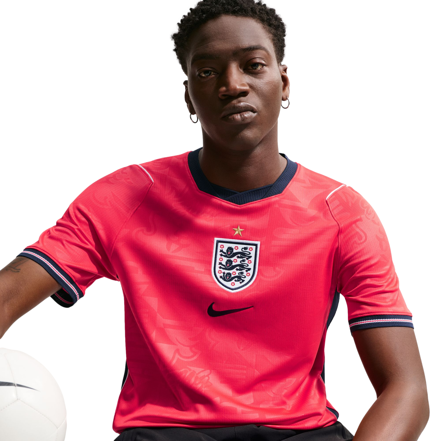 A man wearing a red England national football team jersey with the Three Lions crest and Nike logo, holding a white football against a black background.