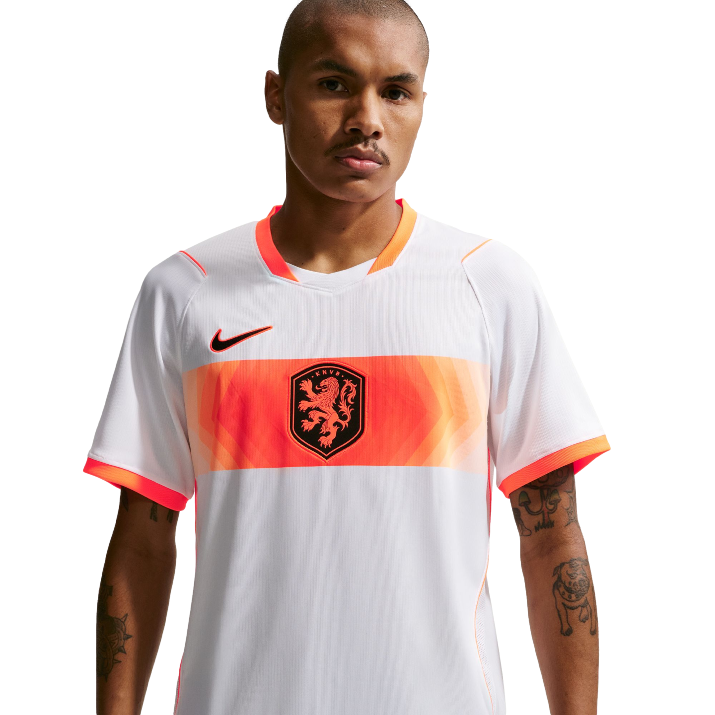 A waist-up portrait of a man wearing a white Netherlands national football team away jersey. The jersey features a wide orange band across the chest with a central lion crest and a black Nike logo on the right. The man has short-cropped hair, a mustache,