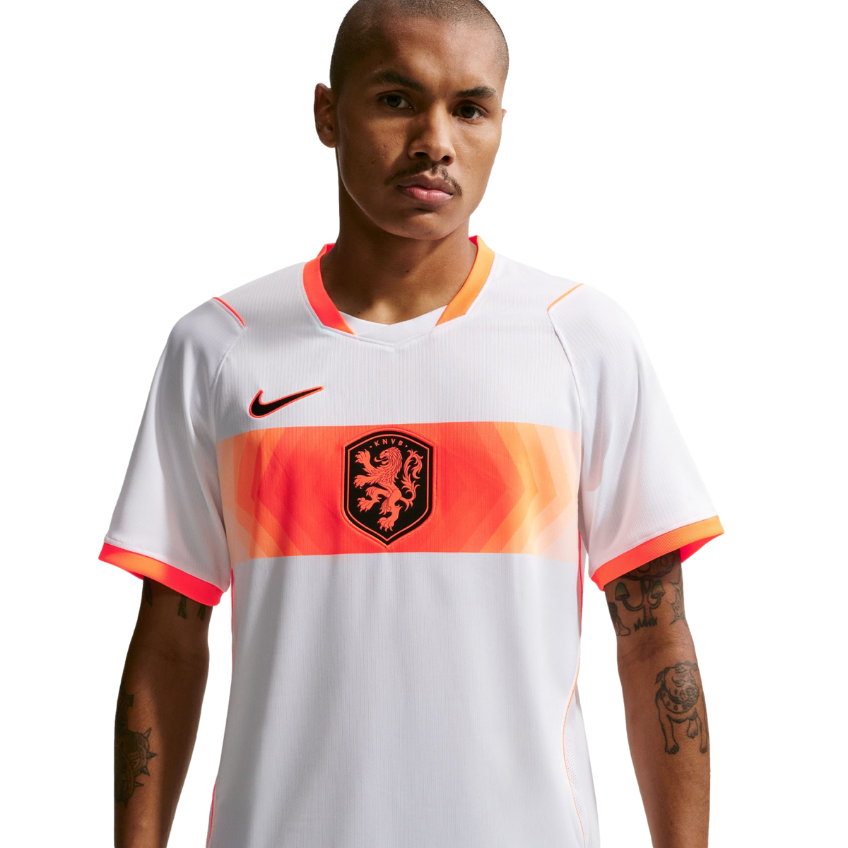 A waist-up portrait of a man wearing a white Netherlands national football team away jersey. The jersey features a wide orange band across the chest with a central lion crest and a black Nike logo on the right. The man has short-cropped hair, a mustache,