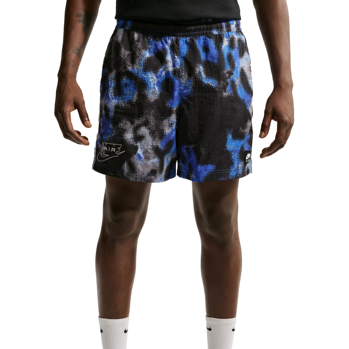 A person wearing Nike athletic shorts with a blue, black, and grey pixelated abstract pattern and white Nike socks, shown from the waist down against a plain white background.