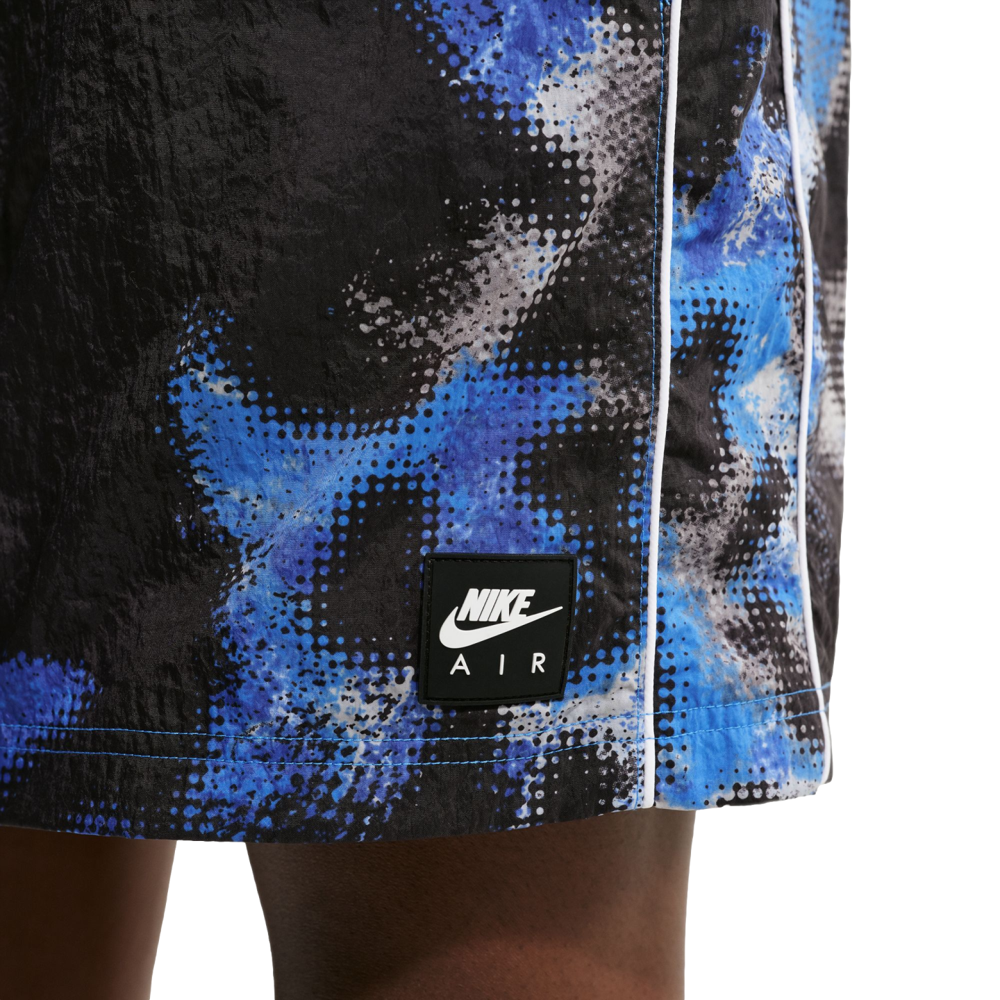 Close-up of Nike Air shorts with a blue and white pixelated graphic on black fabric and a branded patch.