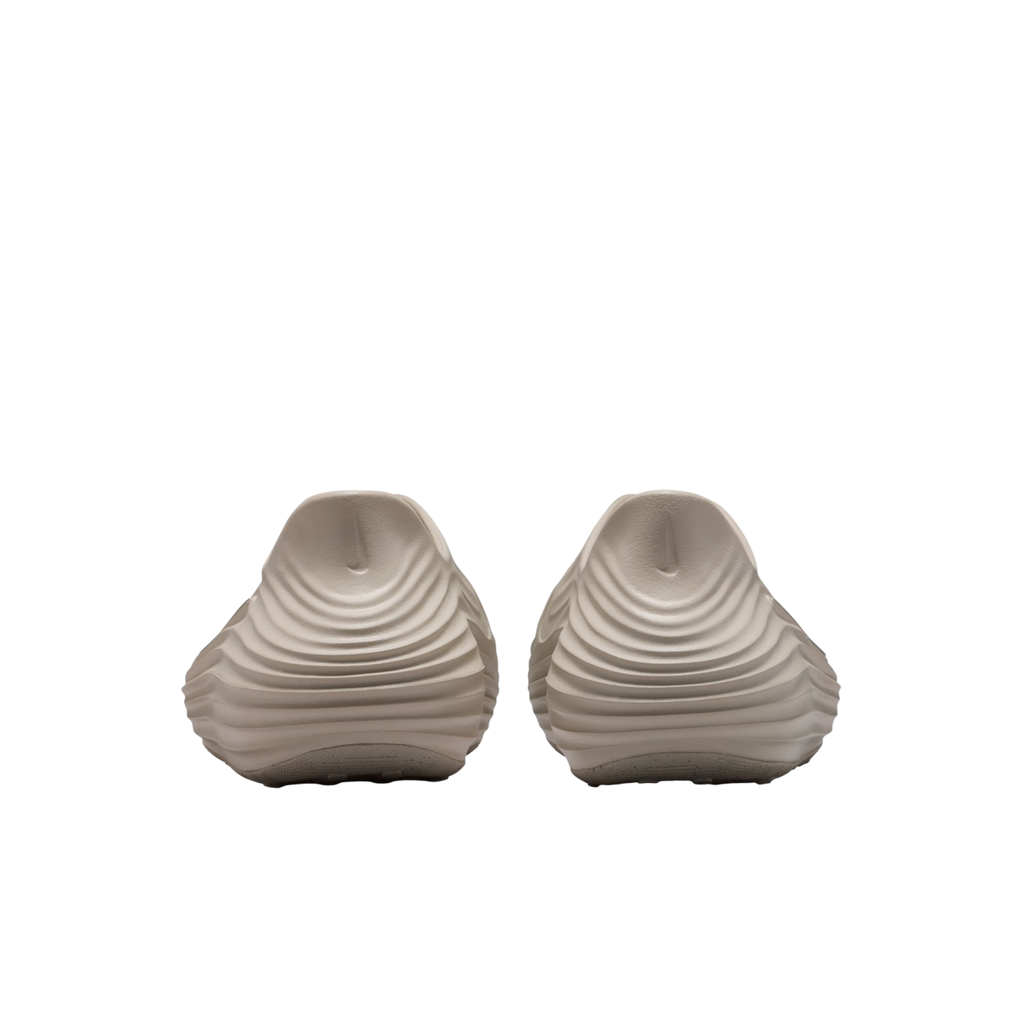 Rear view of two beige slip-on shoes with a unique rippled, wavy texture on the heels and small Nike swoosh logos, presented against a solid black background.