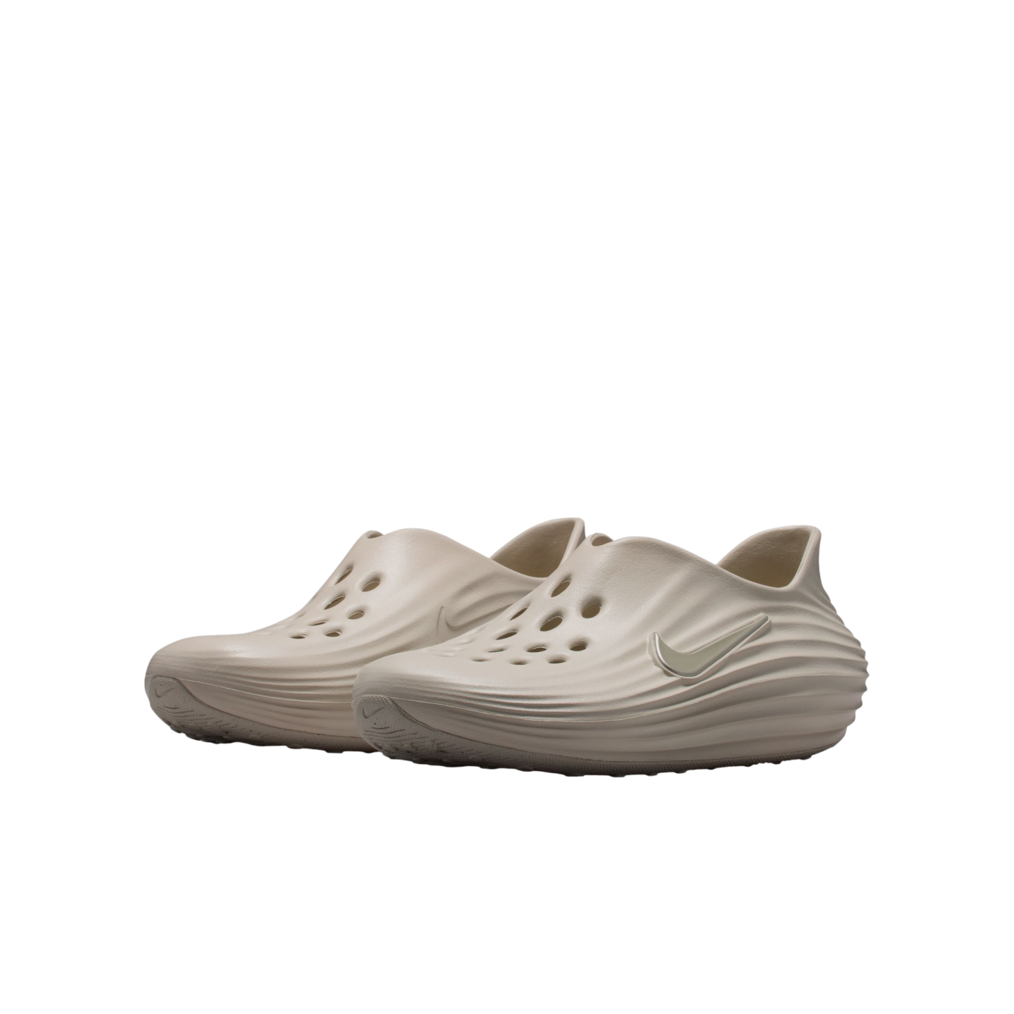 A pair of tan Nike foam clogs featuring perforated holes and wavy textured sides, displayed against a solid black background.