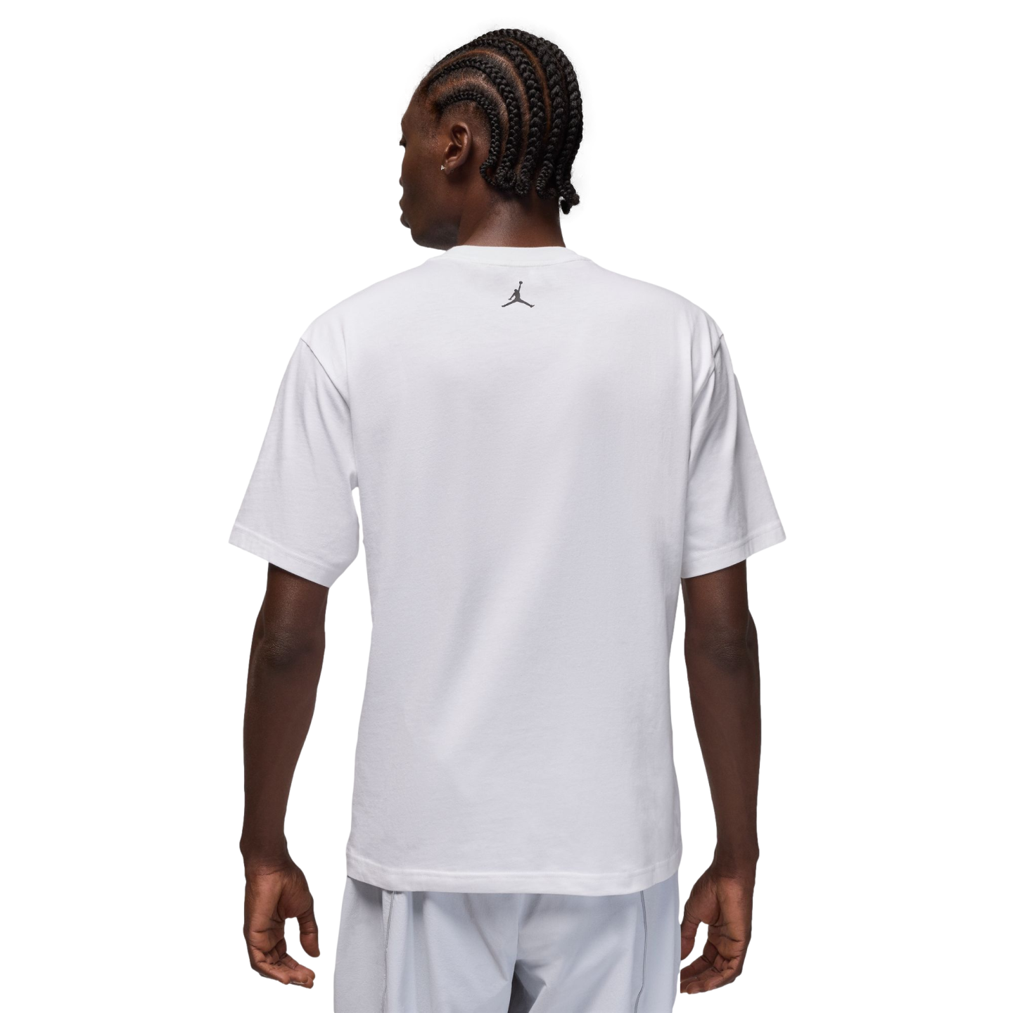 A rear view of a man with braided hair wearing a white t-shirt with a small black logo on the back, set against a black background.