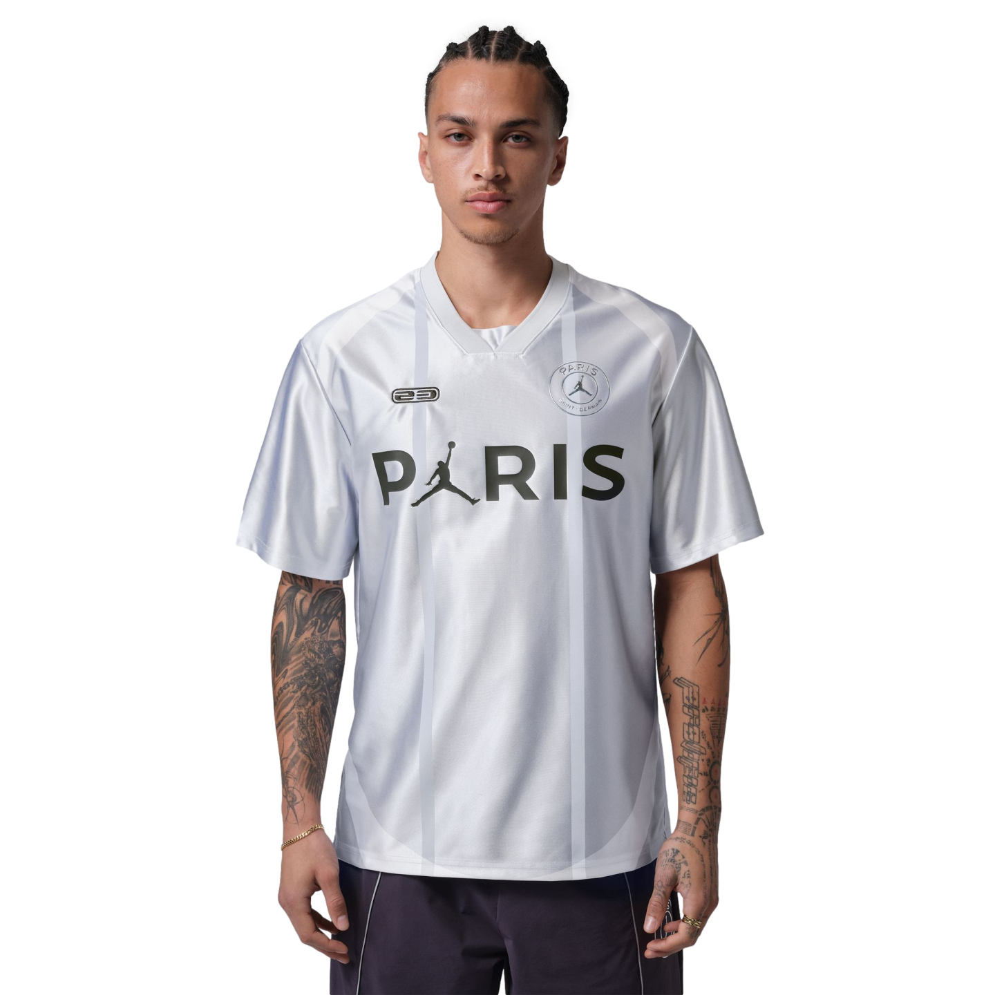 A man with arm tattoos wearing a white Jordan Paris Saint-Germain jersey with "PARIS" across the chest, standing against a black background.