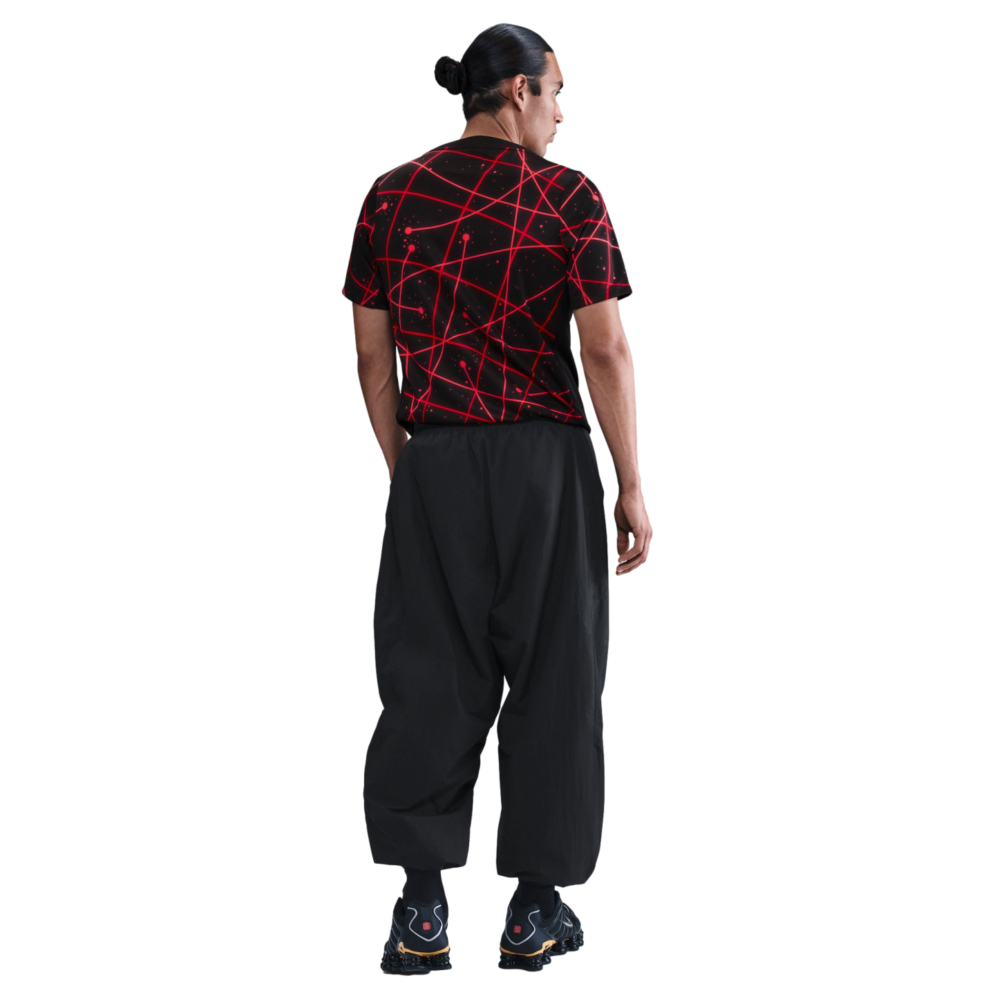 Back view of a man wearing a black t-shirt with a red abstract pattern and baggy black pants against a white background.