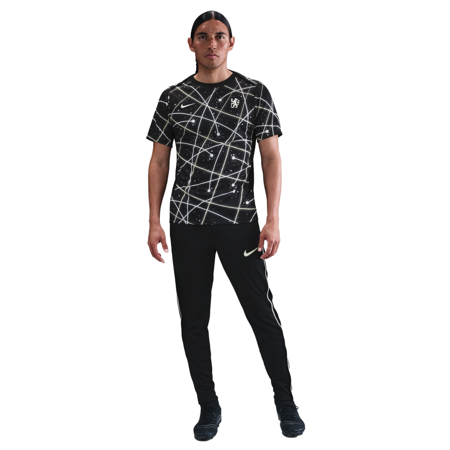 A man stands wearing a black Nike t-shirt with an abstract white geometric pattern and matching black joggers against a plain white background.