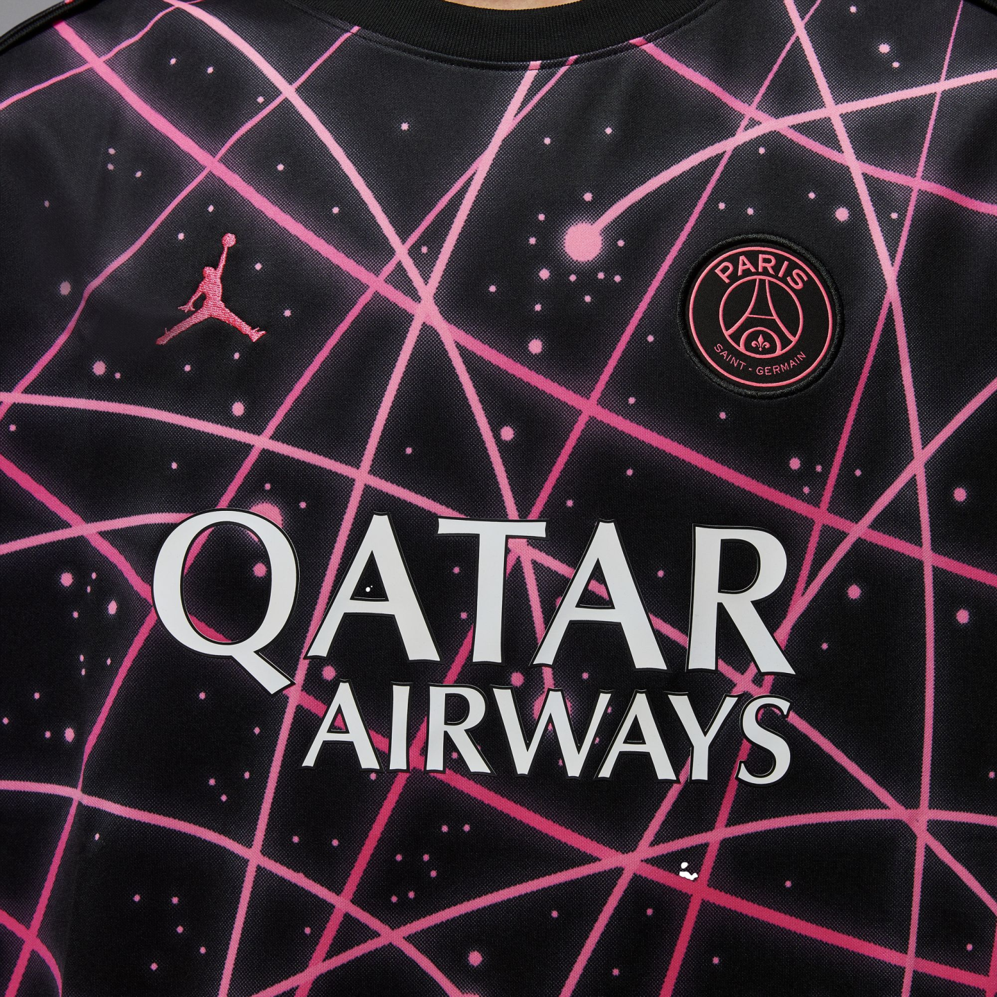A black PSG soccer jersey with a pink neon geometric and starlike pattern. Features the pink Jordan logo, the PSG crest, and the white "QATAR AIRWAYS" sponsor logo.