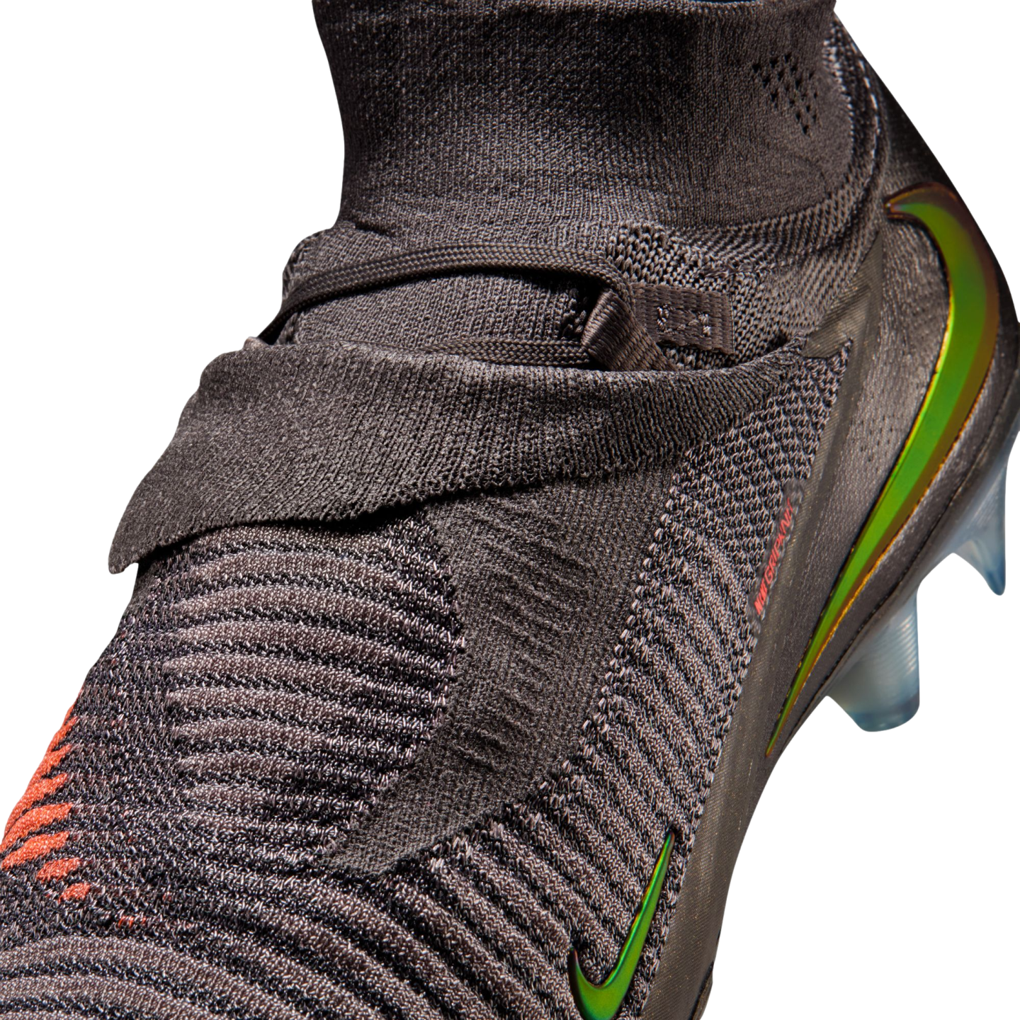 A close-up shot of a dark grey Nike soccer cleat featuring a textured, knitted upper and iridescent green and orange Nike swooshes against a solid black background.