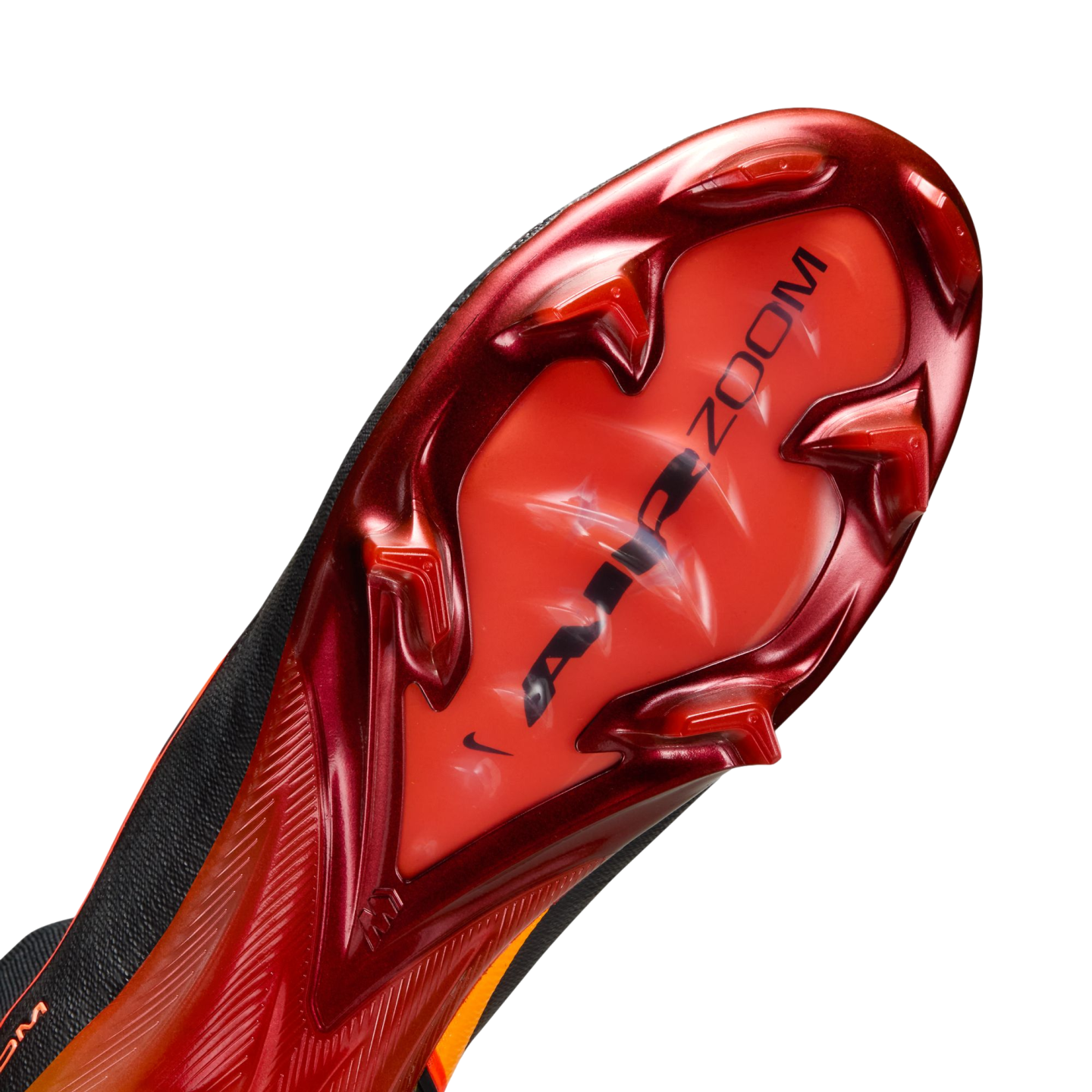 A close-up of the metallic red and orange soleplate of a Nike soccer cleat, featuring chevron-shaped studs and "AIR ZOOM" branding, set against a solid black background.