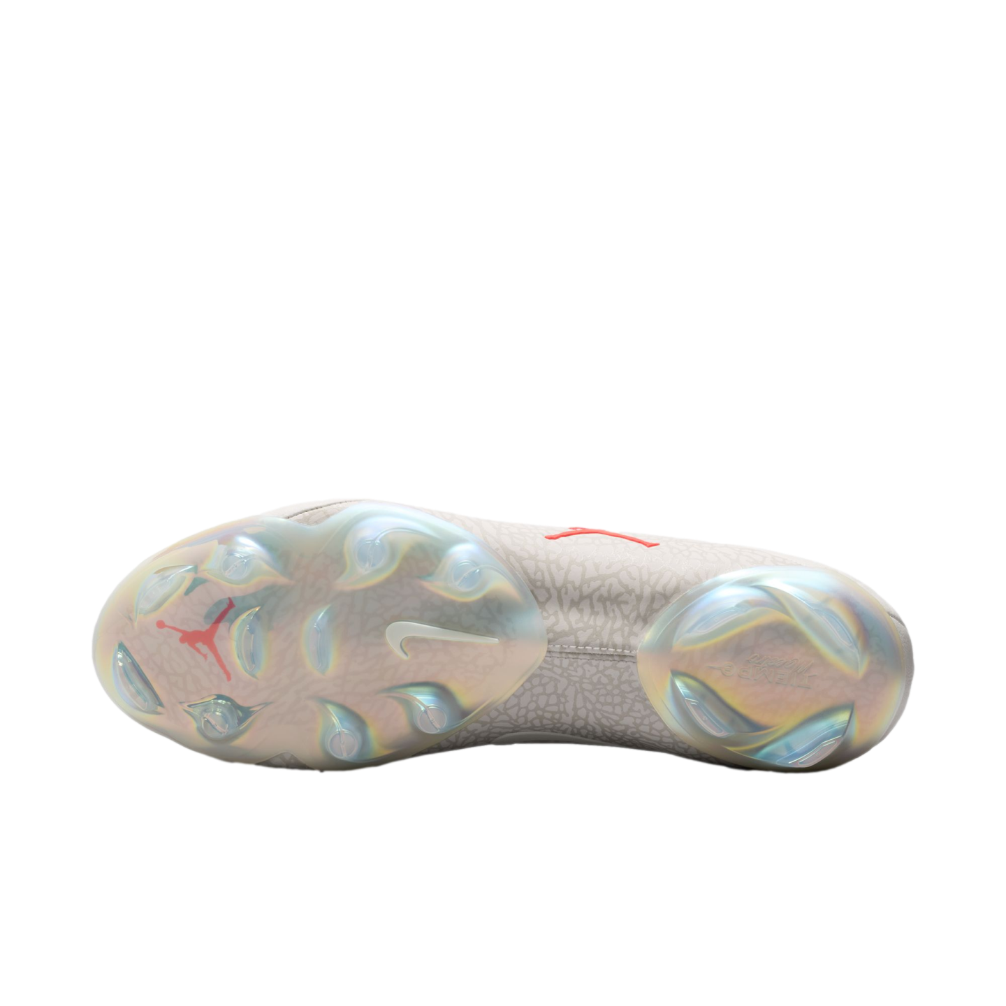 The sole of a Nike x Jordan soccer cleat featuring iridescent plates, molded studs, a red Jumpman logo, and a white swoosh against a gray patterned upper.