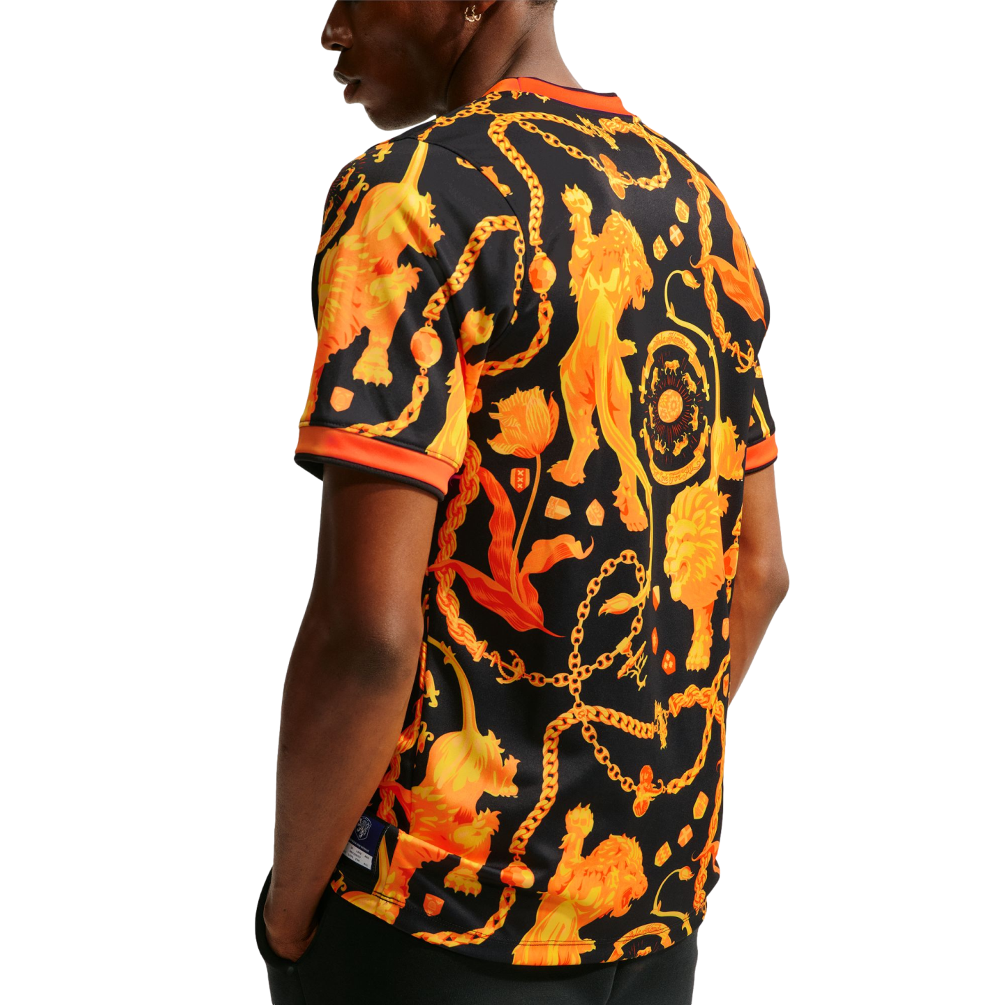 Back view of a person wearing a black t-shirt with an ornate orange pattern of lions, chains, and tulips against a white background.