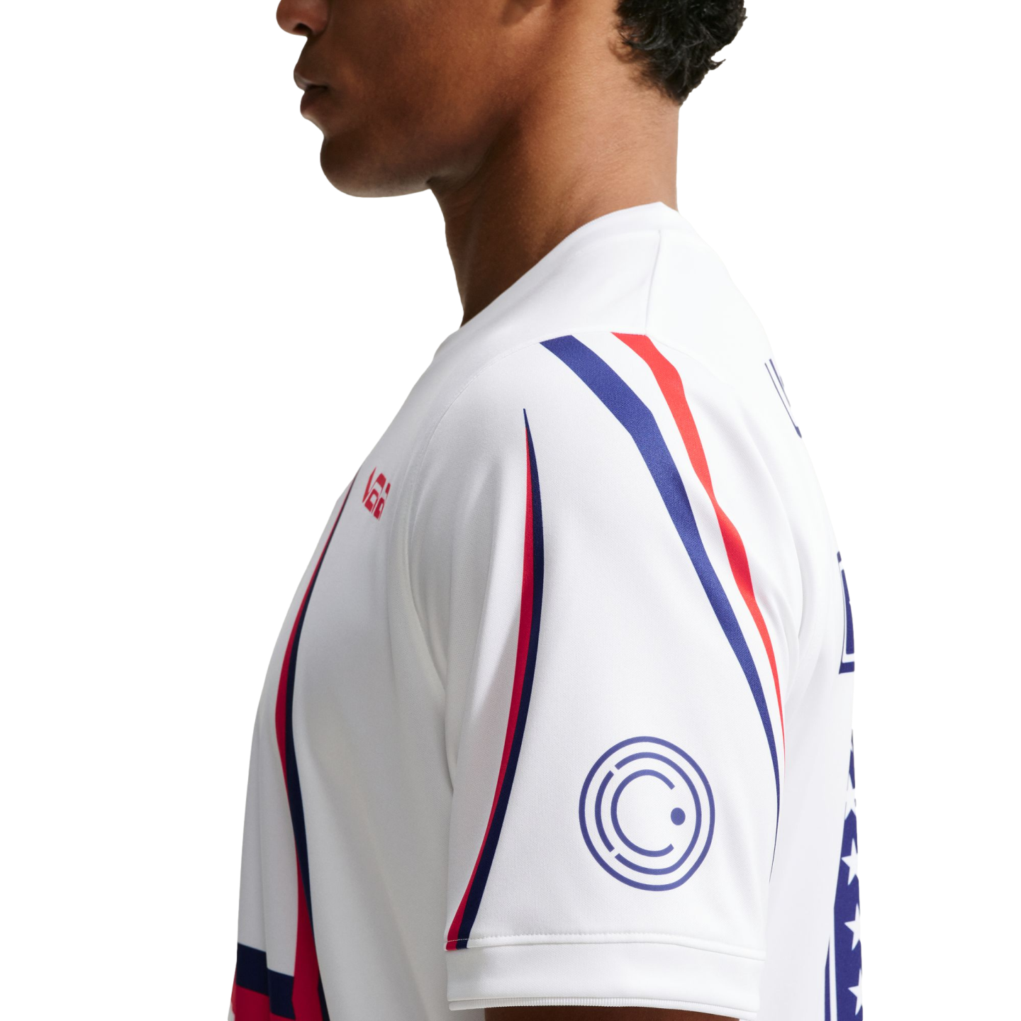 Side profile of a person wearing a white athletic shirt featuring red and blue curved stripes and a circular logo on the sleeve.