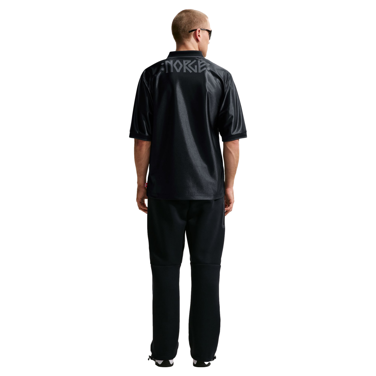 Back view of a man wearing a black jersey with "NORGE" across the upper back and black sweatpants, standing against a white background.