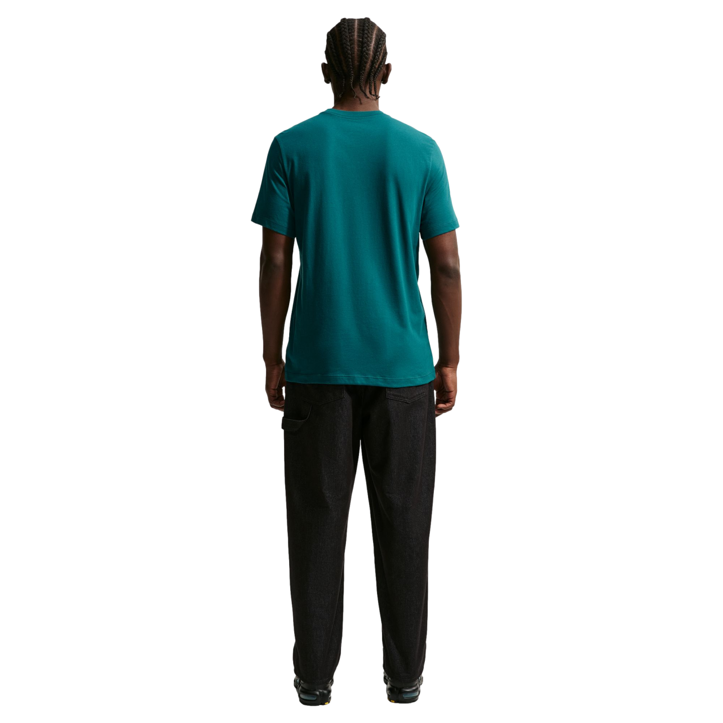 A rear view of a man with braided hair wearing a teal t-shirt and dark, wide-leg pants against a solid black background.