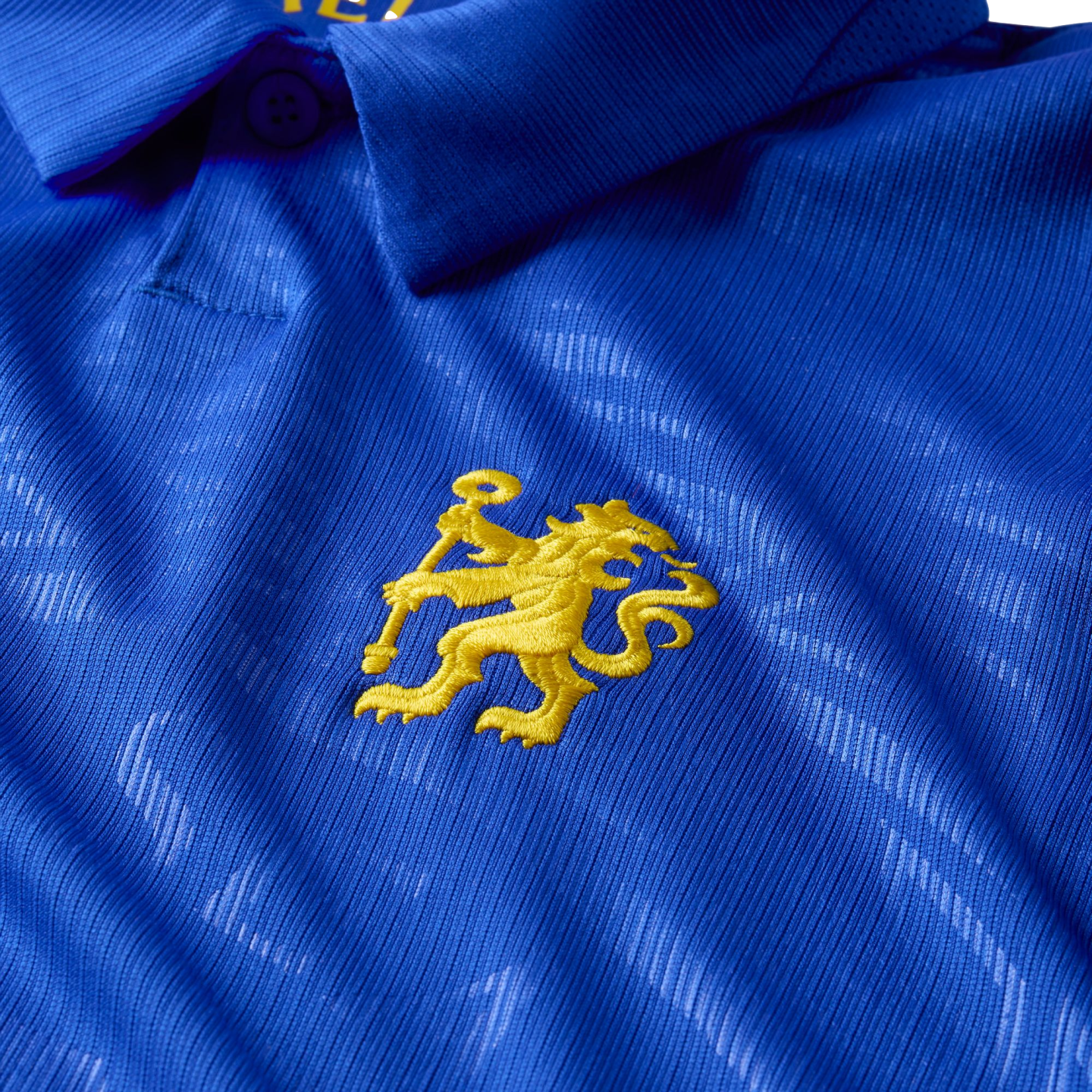 Close-up of a blue textured polo shirt featuring an embroidered yellow lion rampant logo on the chest.