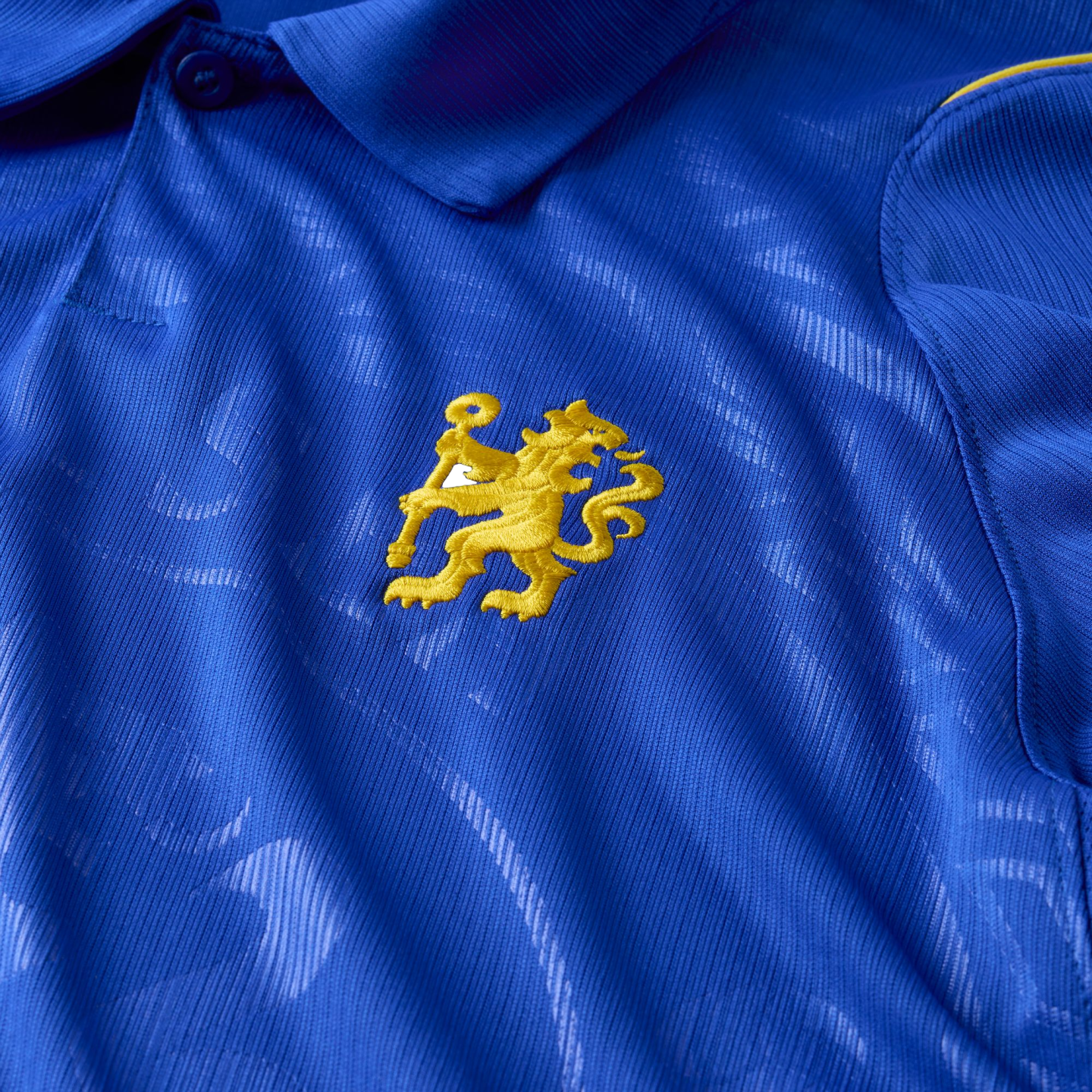 Close-up of a royal blue polo shirt with a yellow embroidered lion logo holding a staff on the chest.